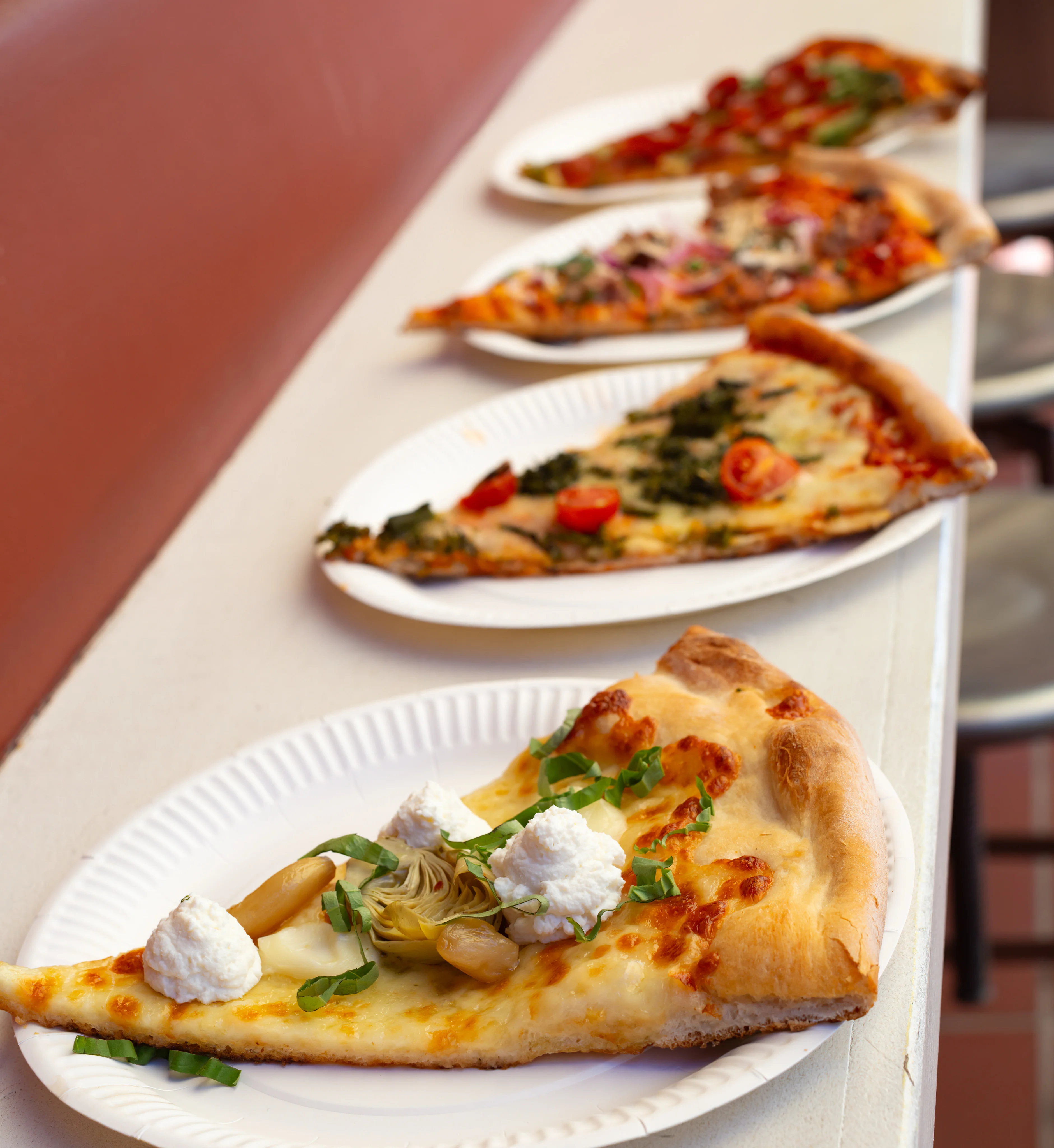 Variety of gourmet pizza slices on paper plates