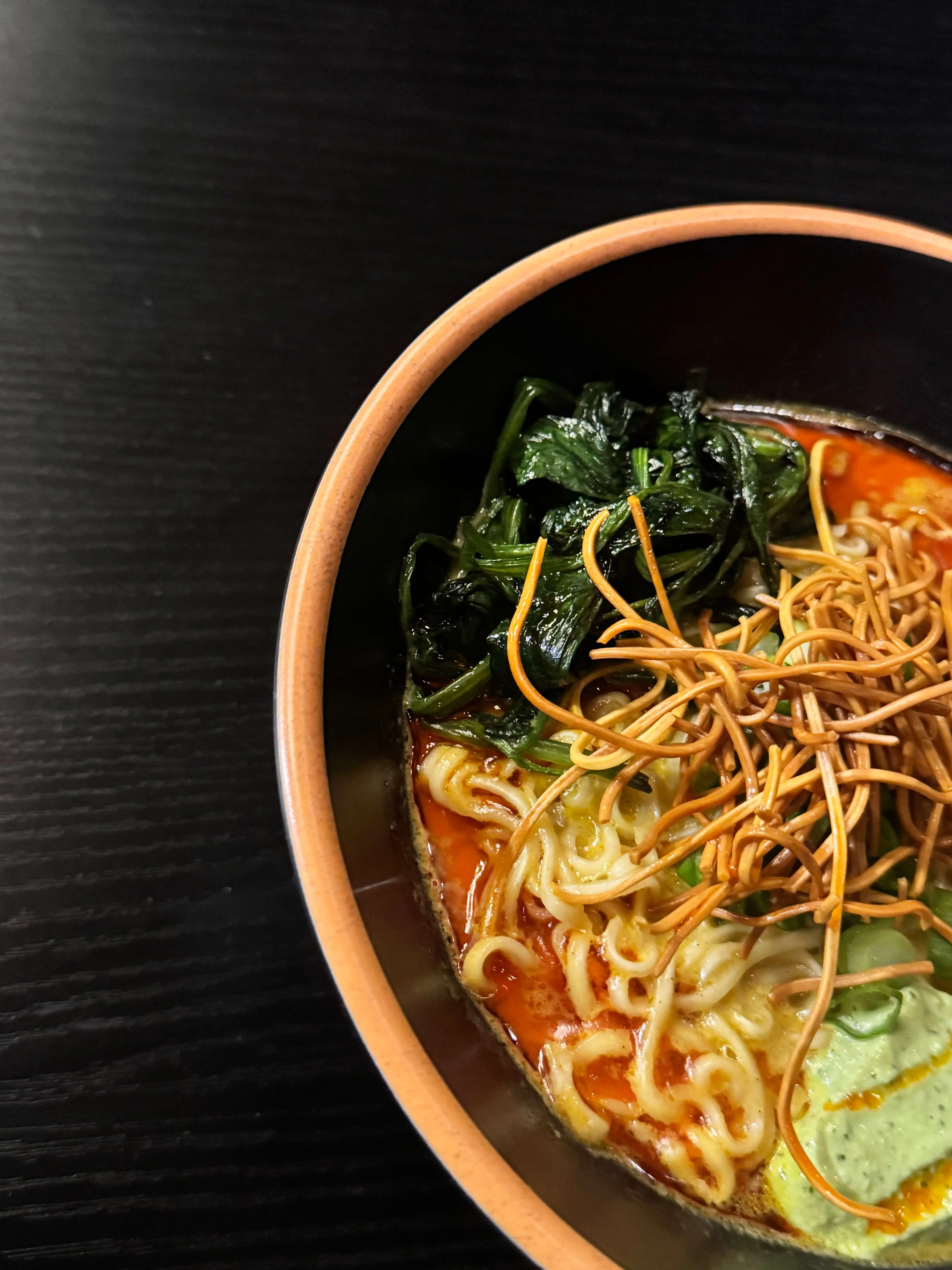 Spicy ramen bowl topped with greens and crispy noodles