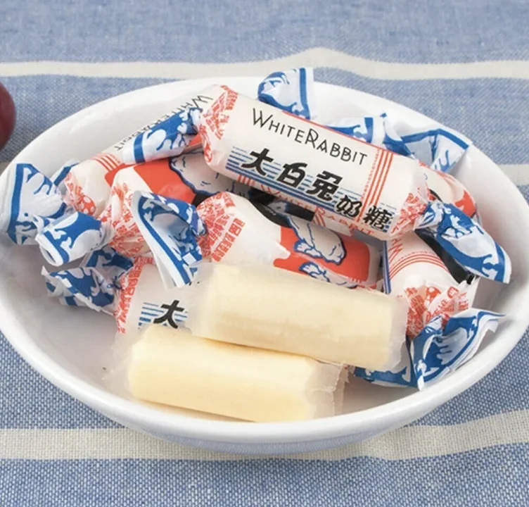 A bowl filled with various wrapped candies, prominently featuring a design with a white rabbit. The candies are primarily white and red.