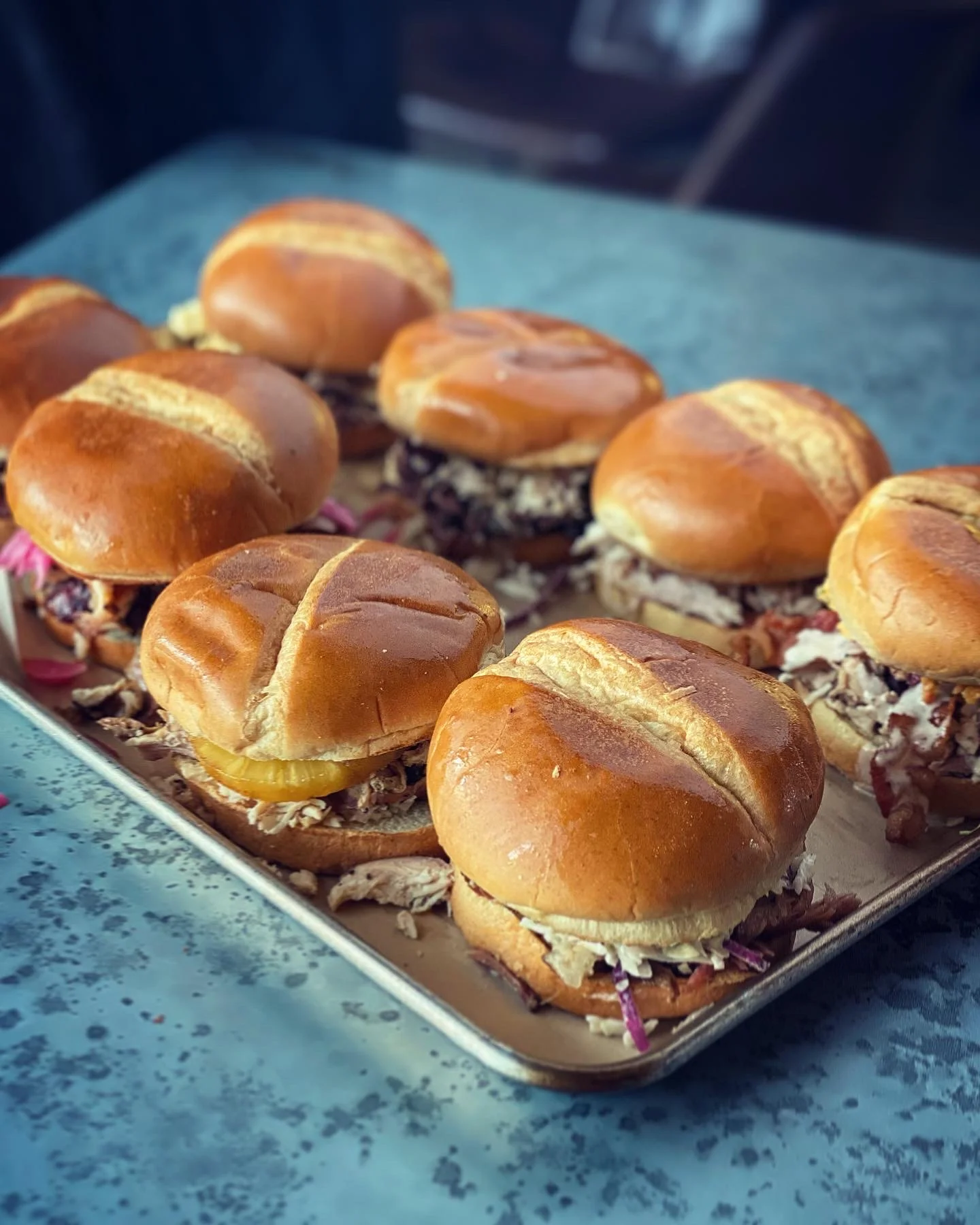 A tray filled with several pulled pork sandwiches topped with coleslaw and pickles.