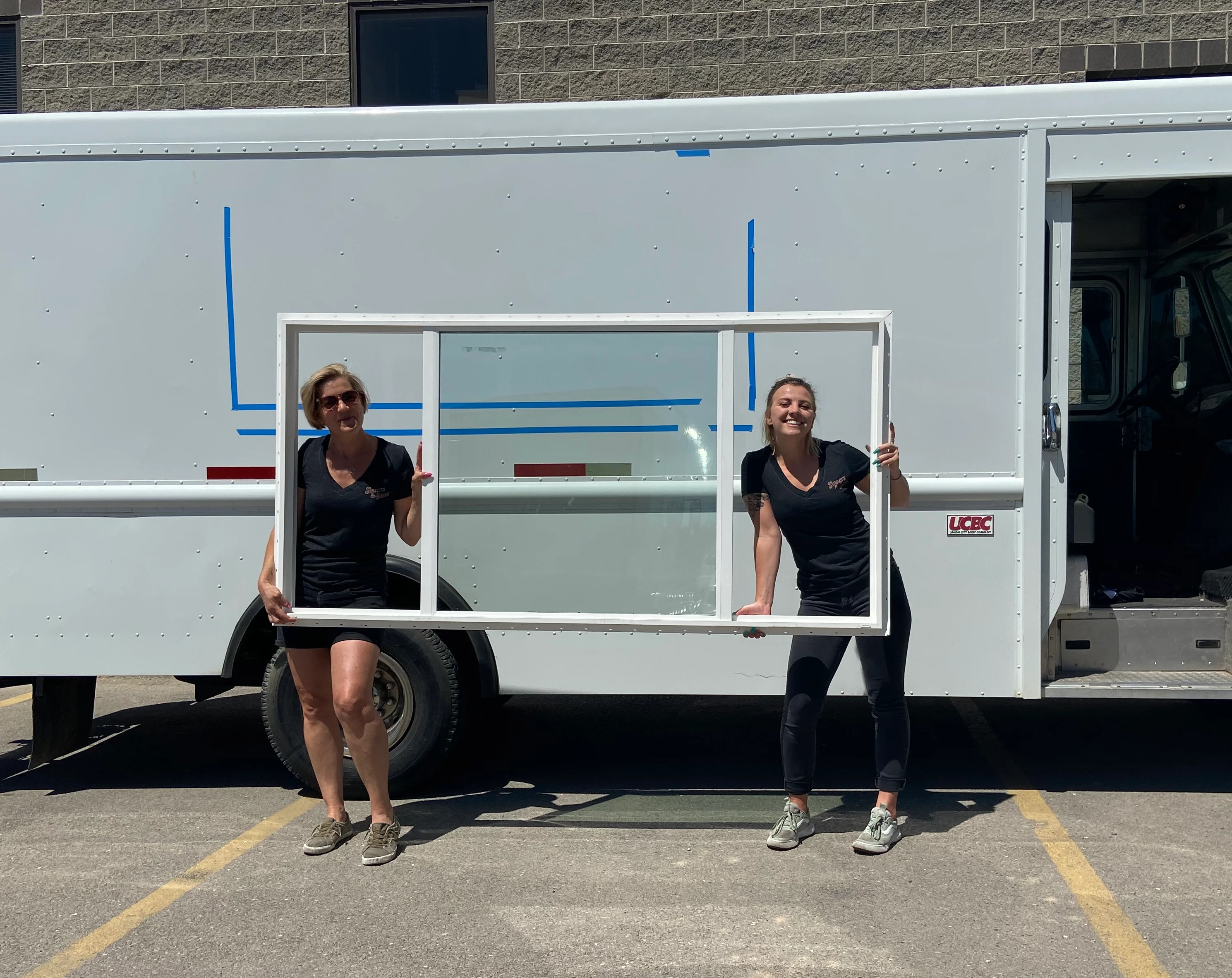 Two women holding a window frame in front of a food truck