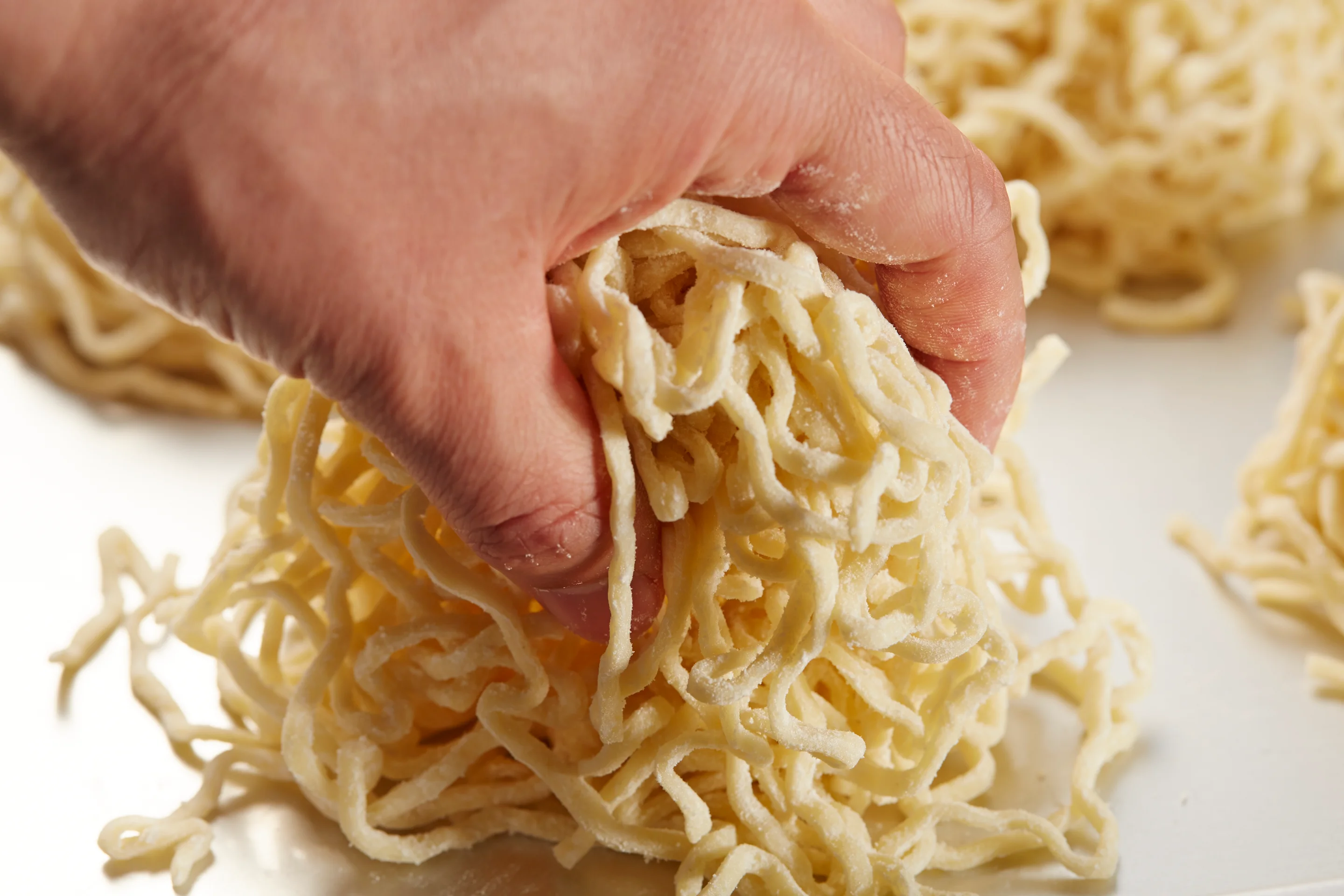 A bowl of ramen noodles being lifted with chopsticks, showcasing broth, pork slices, green onions, and bamboo shoots.