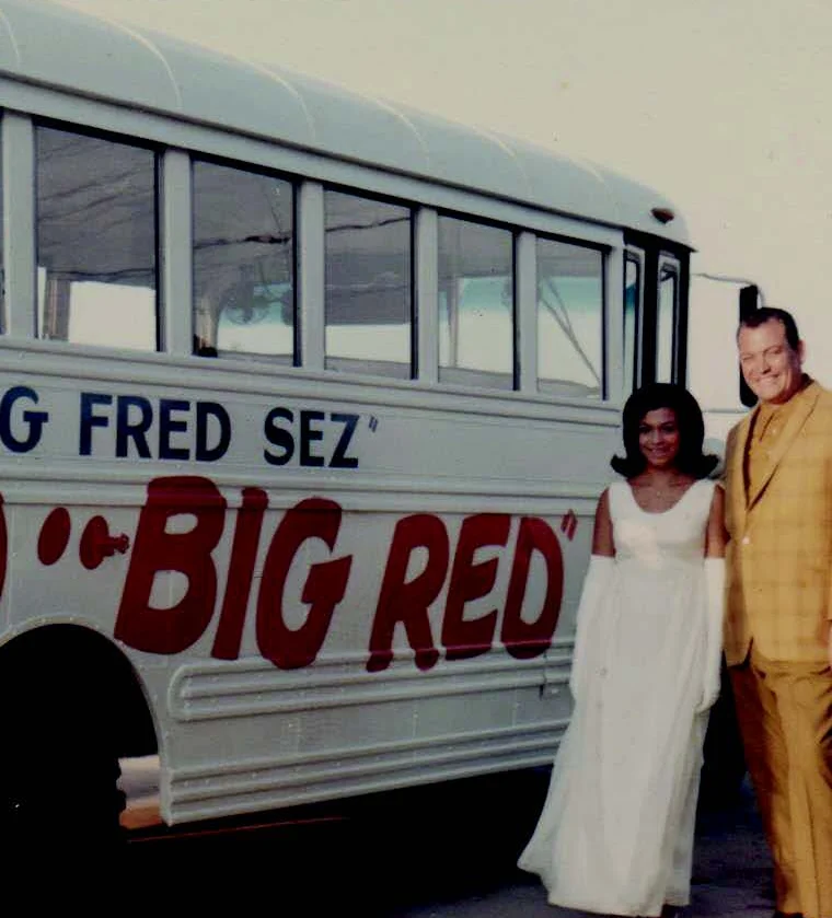 Couple posing by a vintage bus with 'Big Fred Sez' signage