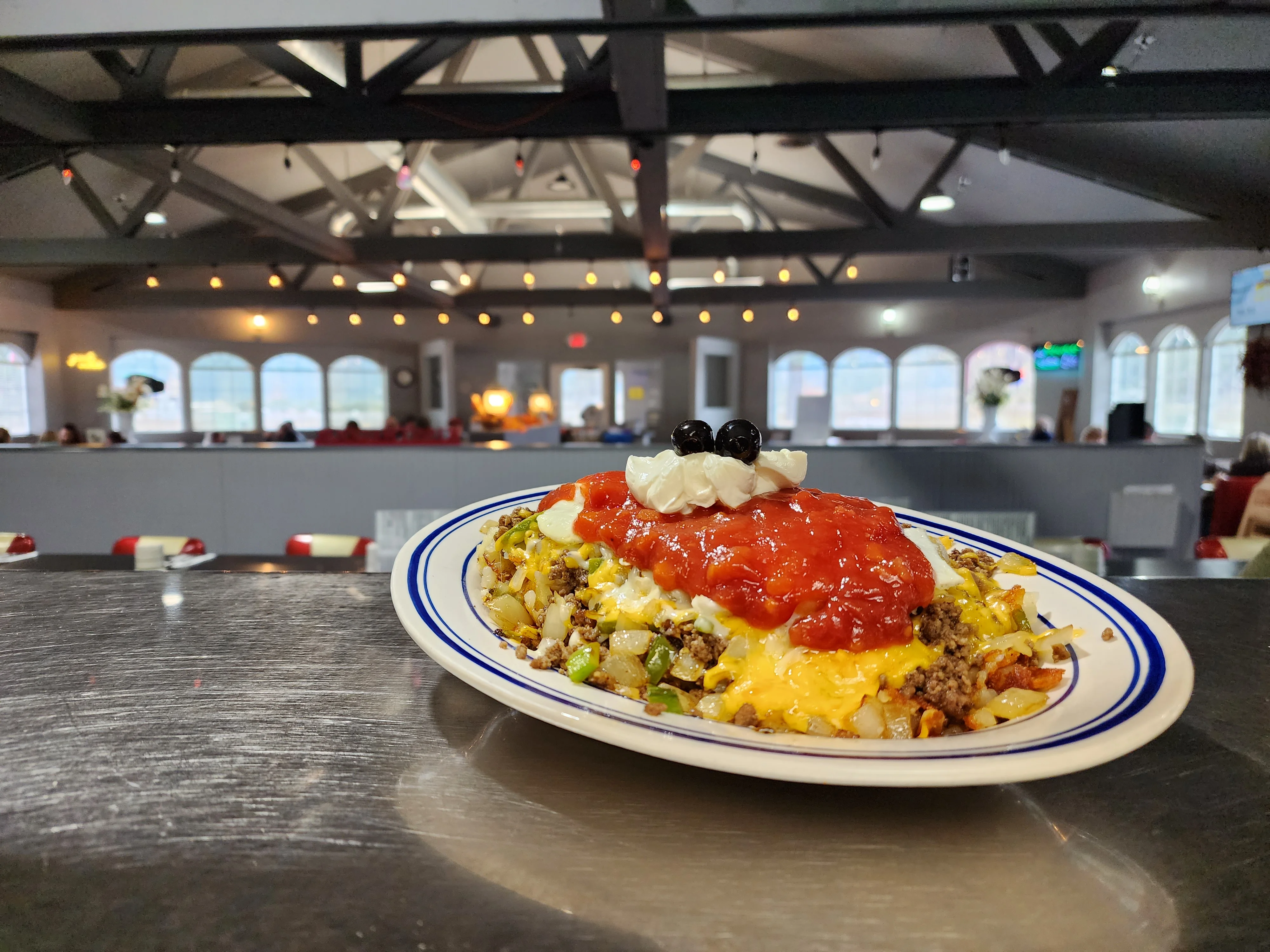 A colorful dish featuring seasoned ground beef, topped with cheese, salsa, and whipped cream, served on a white plate with blue trim.