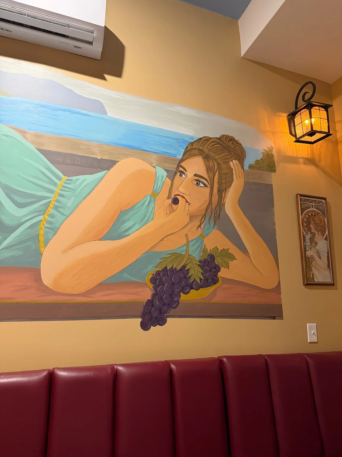 Hand-painted mural of a woman with grapes above the red seating at Villa Italiana