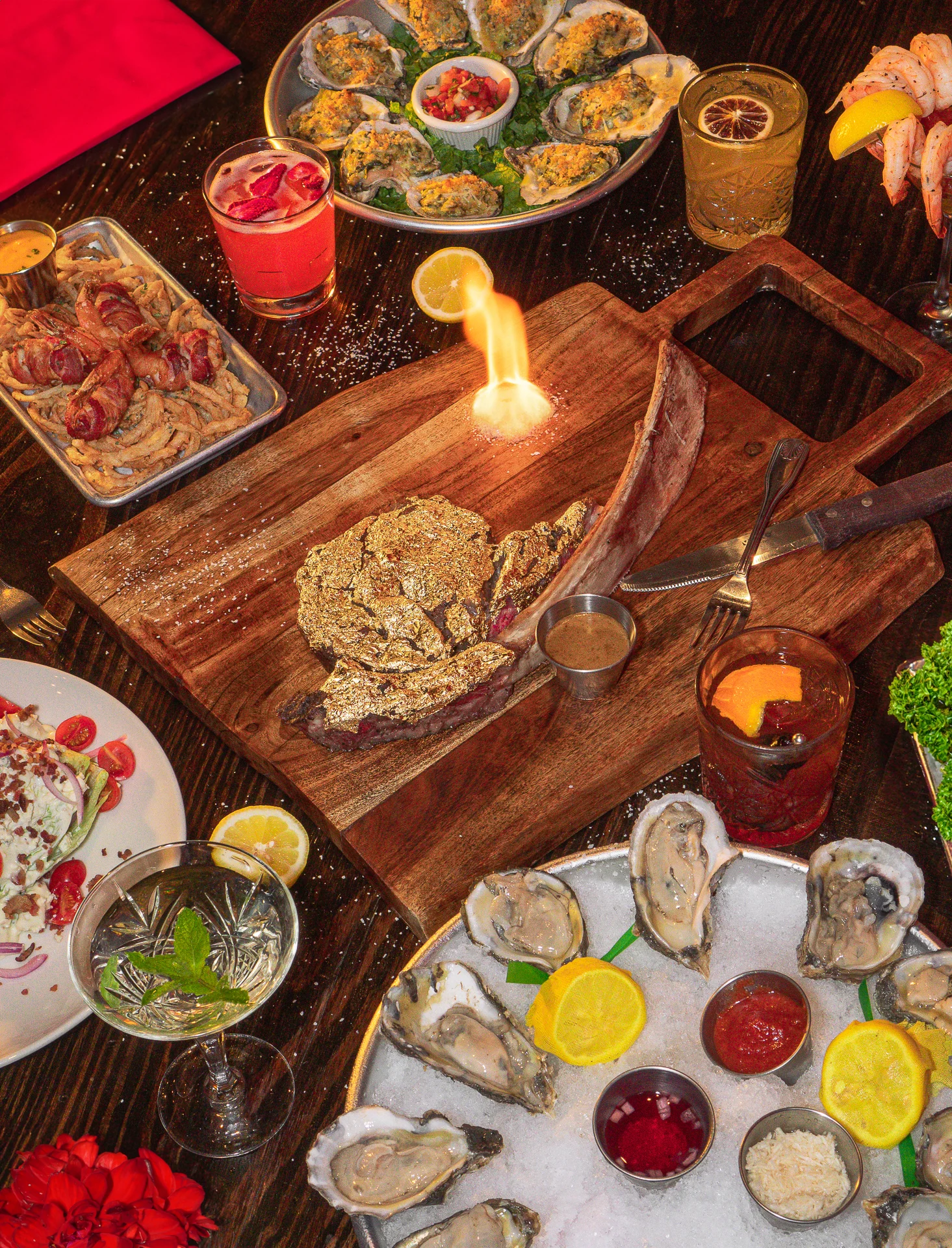 Pour Behavior’s upscale dinner spread featuring a gold-crusted tomahawk steak with live fire, fresh oysters, shrimp cocktail, bacon-wrapped bites, and signature cocktails.