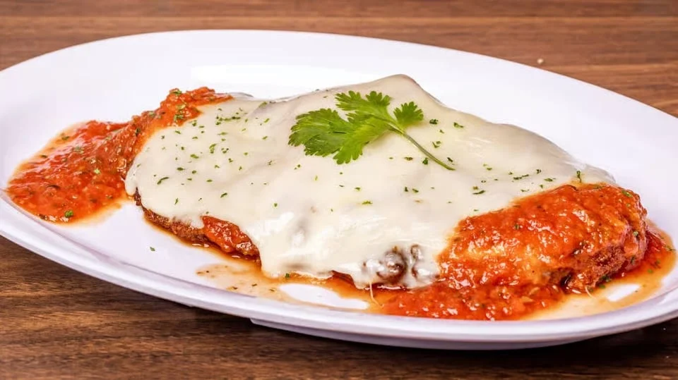 Breaded chicken parmigiana topped with melted mozzarella and tomato sauce, served on a white plate.