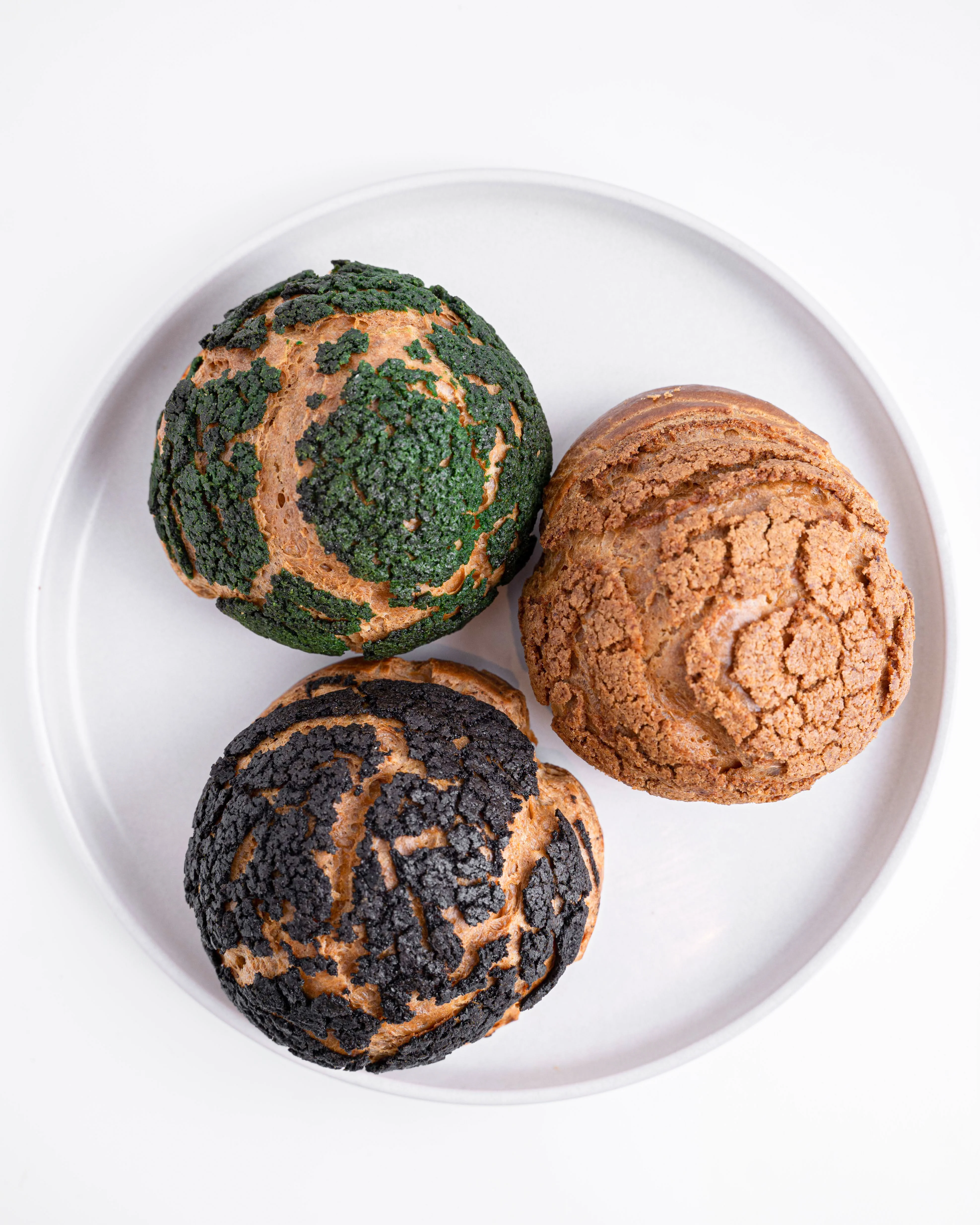 A plate featuring three different varieties of textured buns, each with unique colors and patterns.