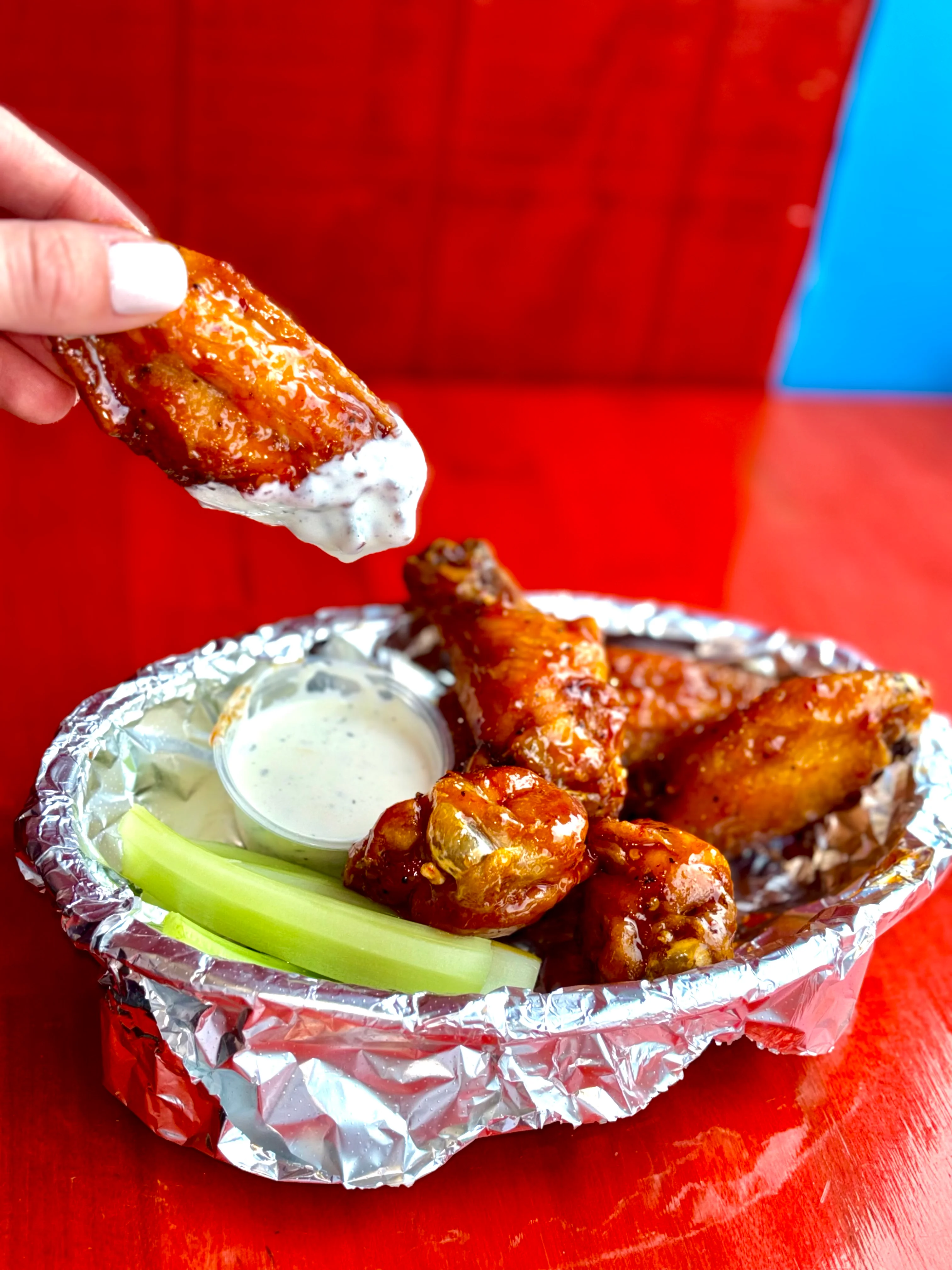 A close-up of a plate with chicken wings accompanied by celery sticks and a dipping sauce.