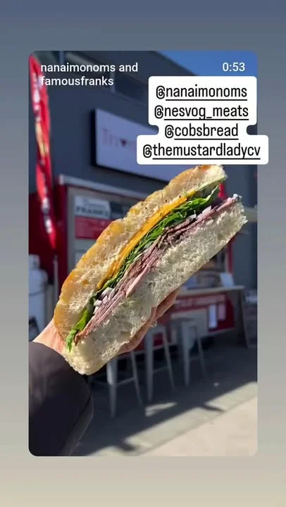 A hand holding a sandwich filled with layers of meat, greens, and cheese, showcasing a fresh bread exterior.