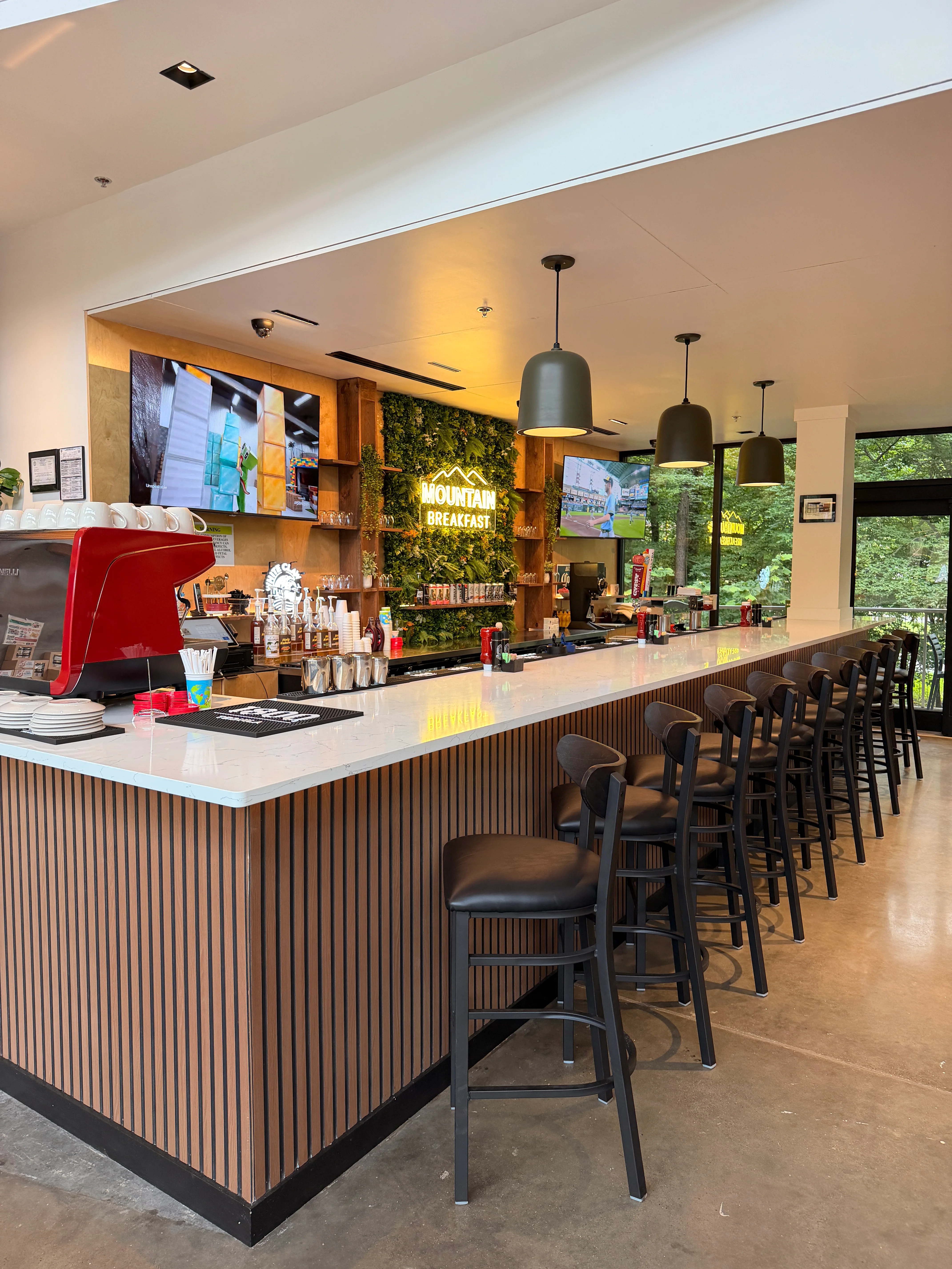 A bar area with a counter, drinks on display, and a sign reading 'Mountain Breakfast,' surrounded by chairs.
