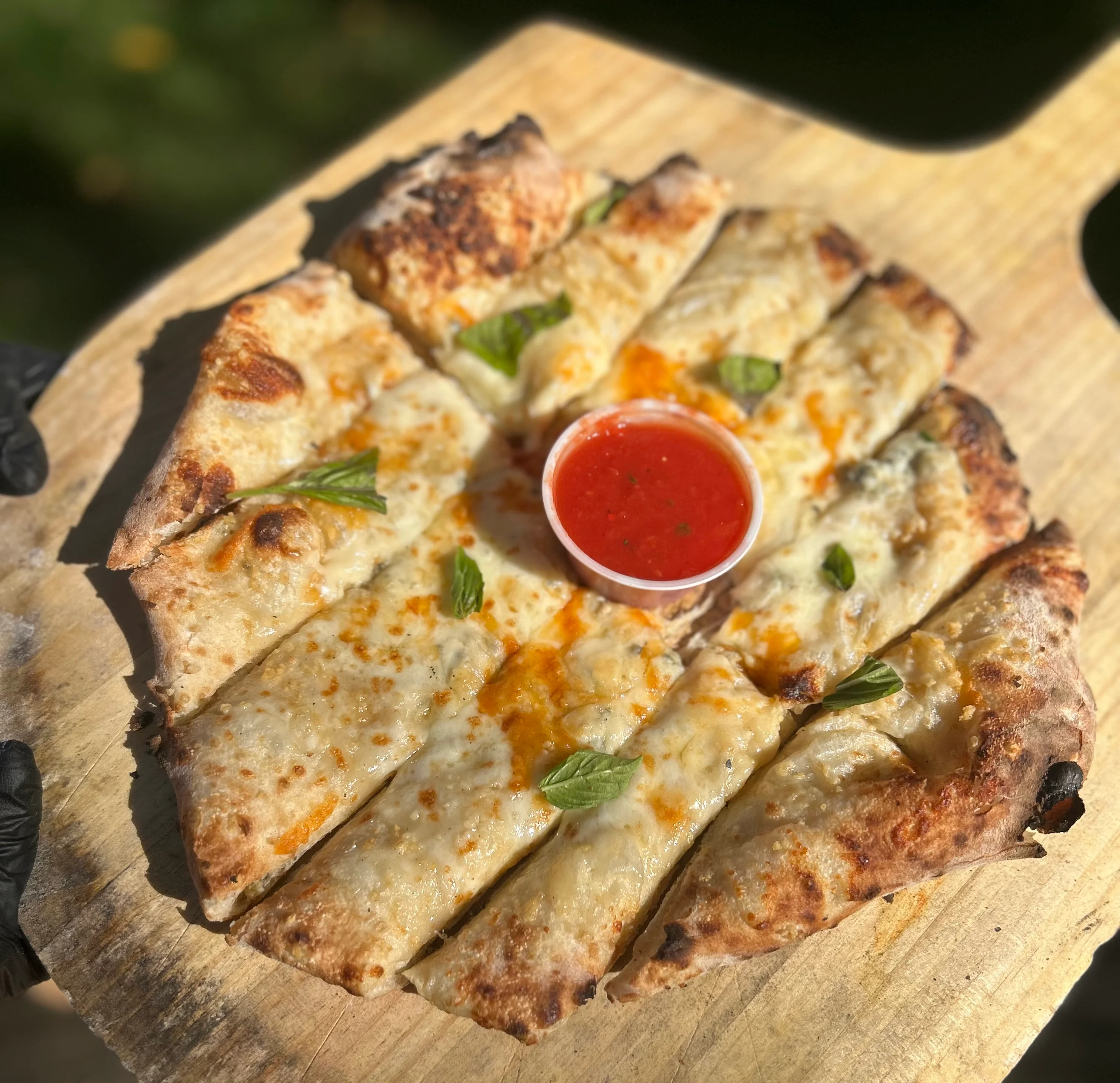 Cheesy pizza slices on a wooden board with dipping sauce