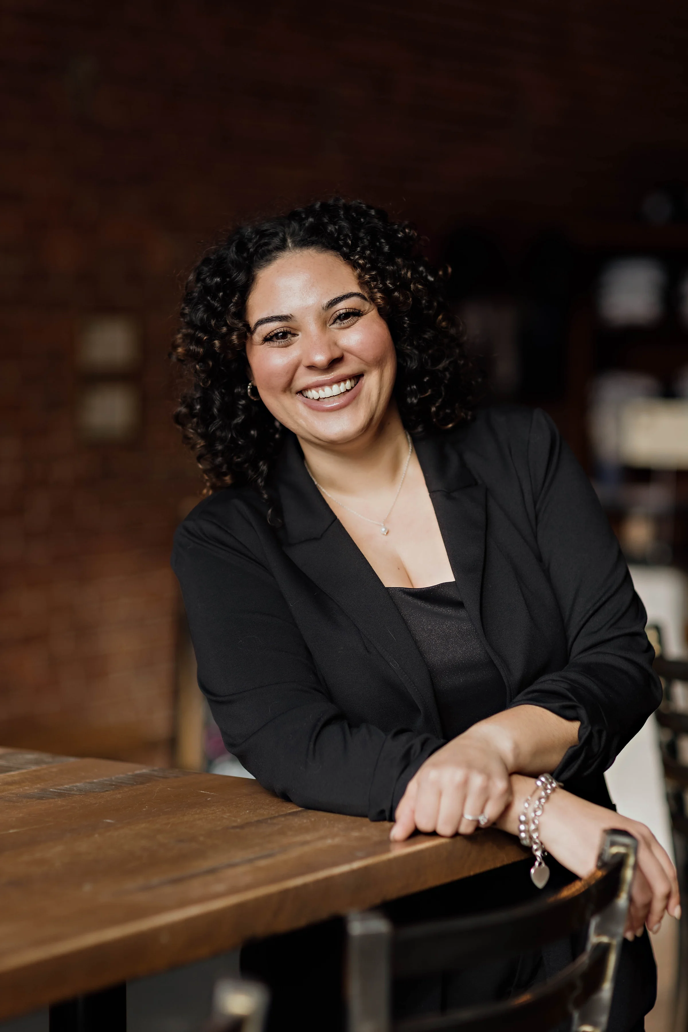 Smiling woman in a black blazer at a rustic restaurant setting
