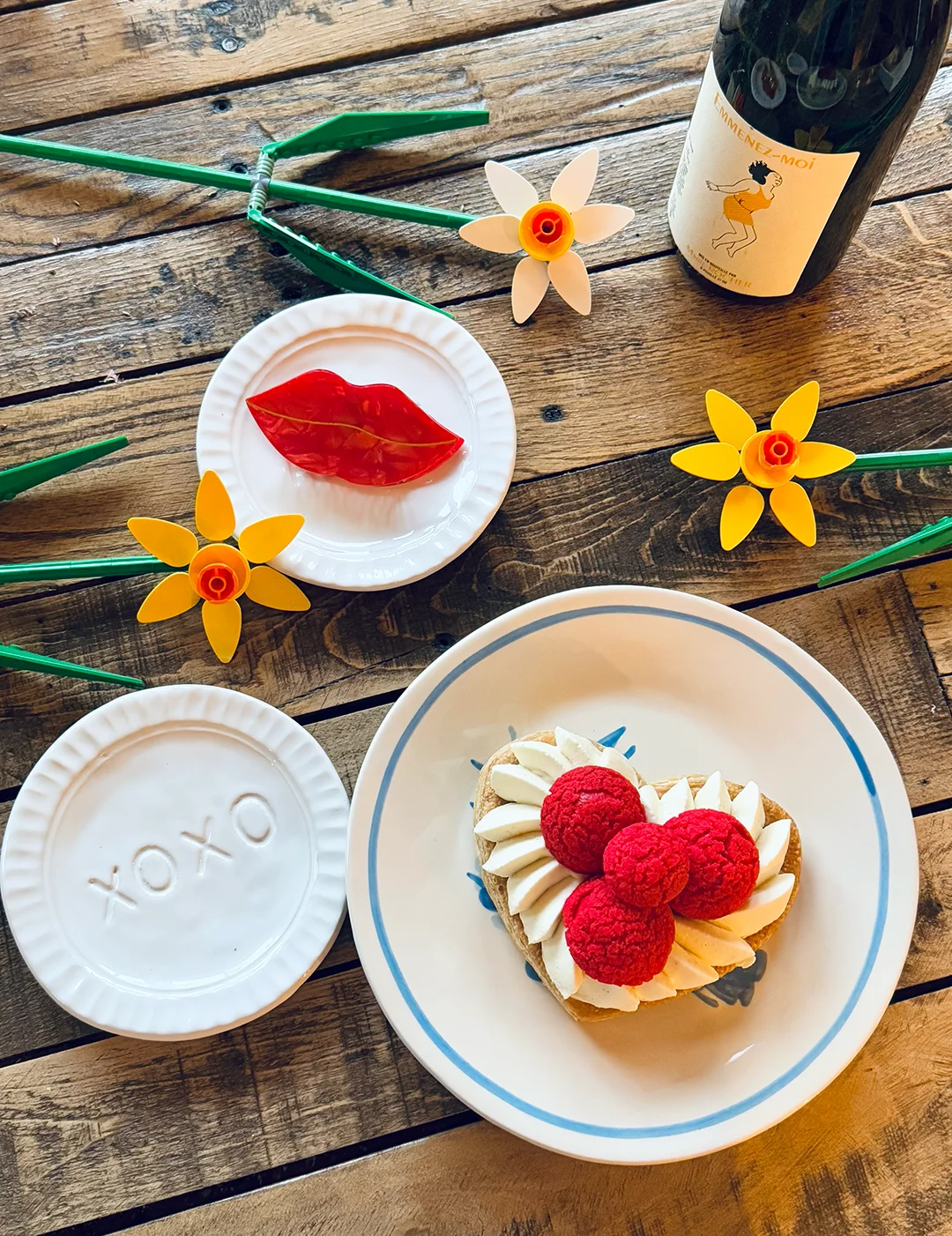 Heart-shaped Raspberry Blush St-Honoré on a plate with “xoxo,” surrounded by Lego flowers and a bottle of wine, creating a warm, cozy Valentine’s Day café vibe