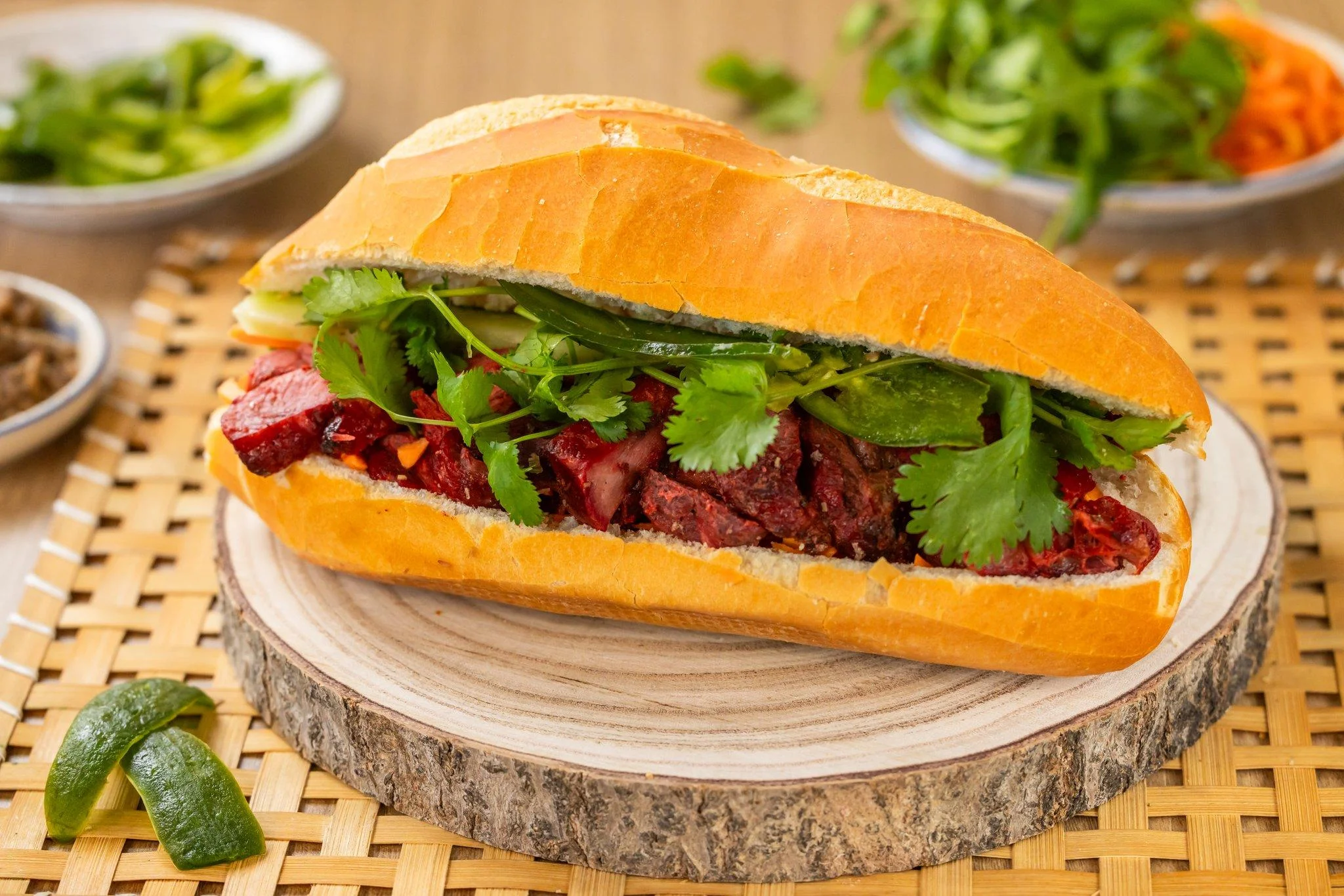 A delicious sandwich filled with meat, fresh vegetables, and cilantro, served on a crusty baguette-style bread.