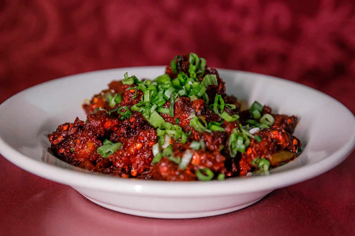 A delicious bowl of classic Chicken Tikka Masala from Mint Indian Restaurant, featuring a rich, creamy tomato sauce and a garnish of fresh cilantro.