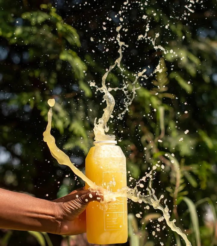 Refreshing yellow juice splashing from a bottle in a vibrant outdoor setting