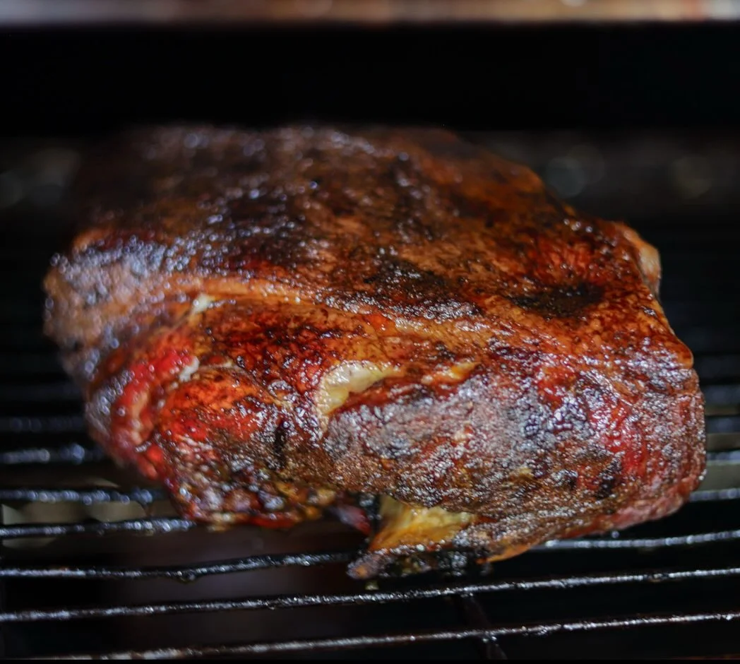 A large piece of smoked meat on a grill, showcasing a rich, dark crust and juicy texture.