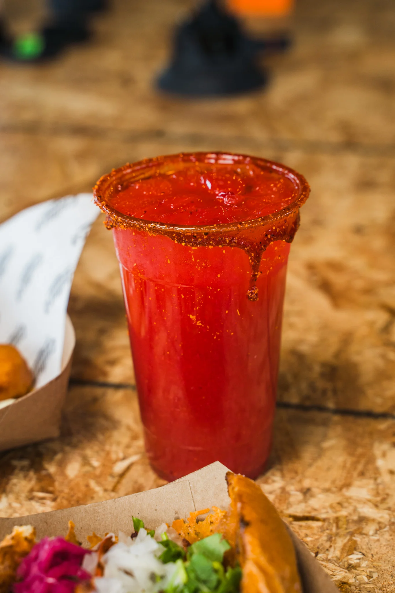 A vibrant red drink with a spicy rim, served in a clear cup.