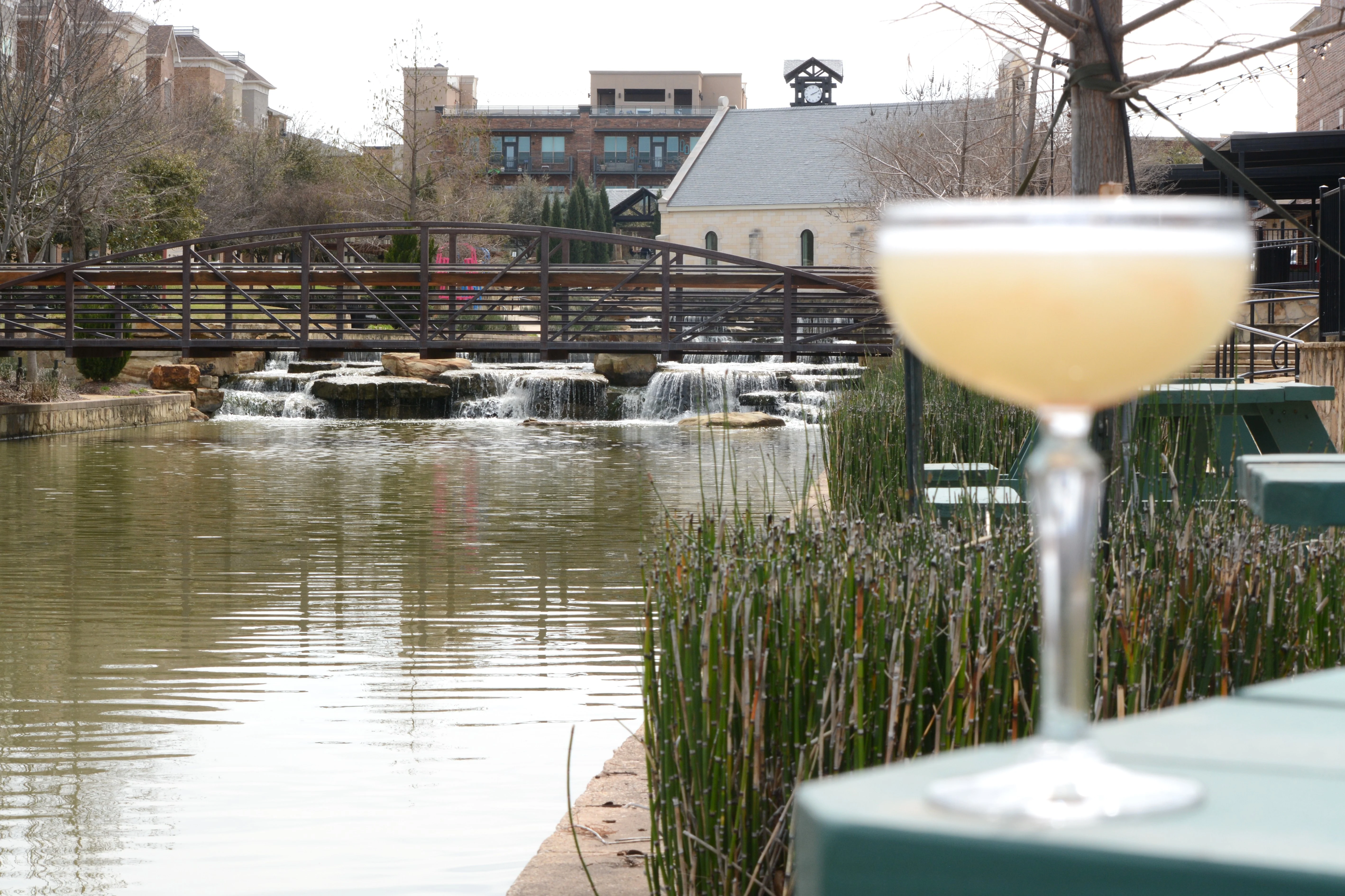 Cocktail by a serene pond with a bridge and waterfall