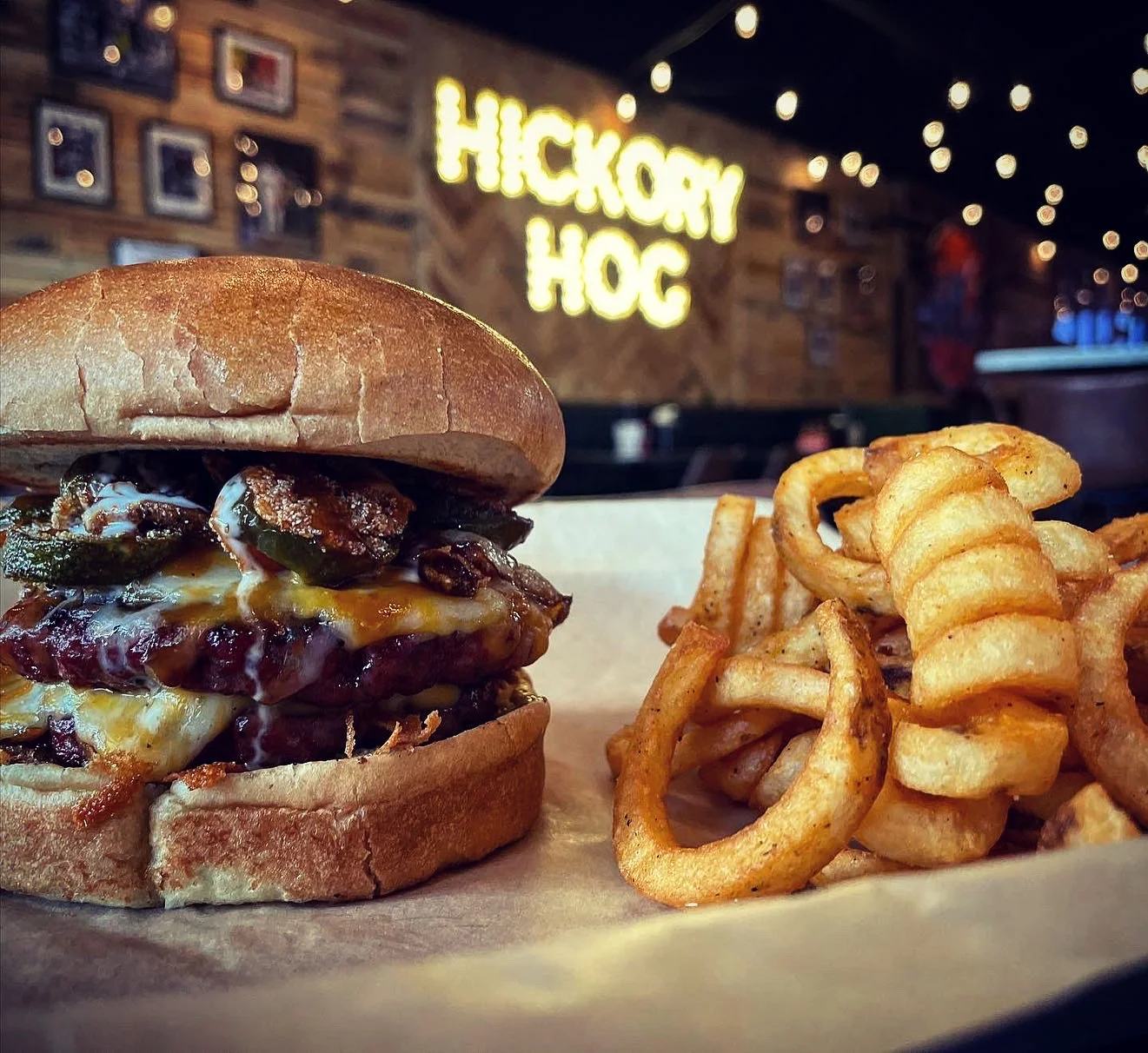 A gourmet burger with melted cheese and jalapeños served alongside curly fries, set against a restaurant backdrop.