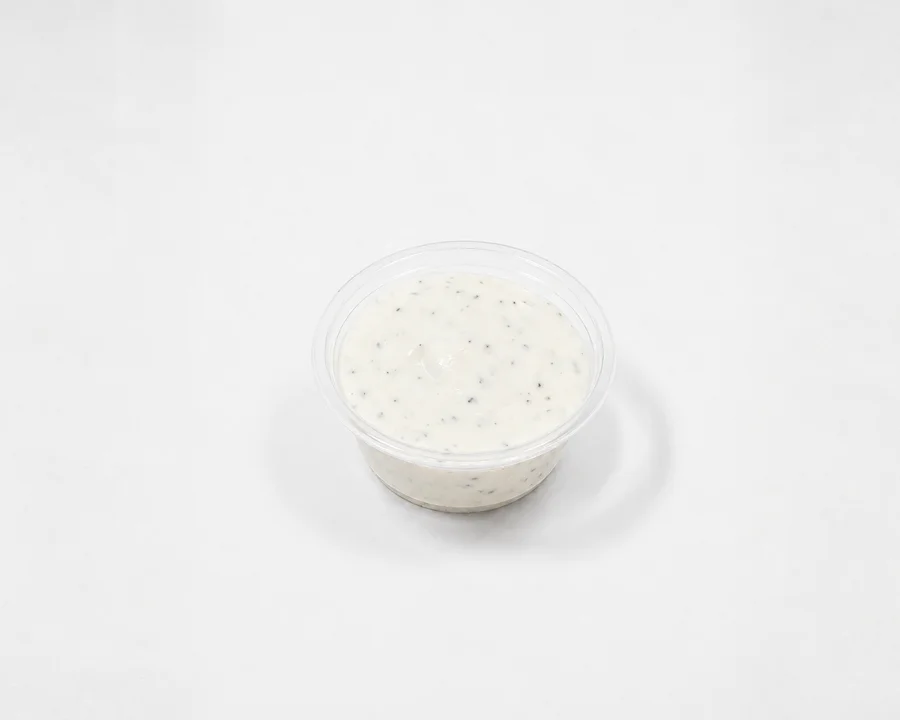 A small container of creamy dipping sauce with herbs flecked throughout.