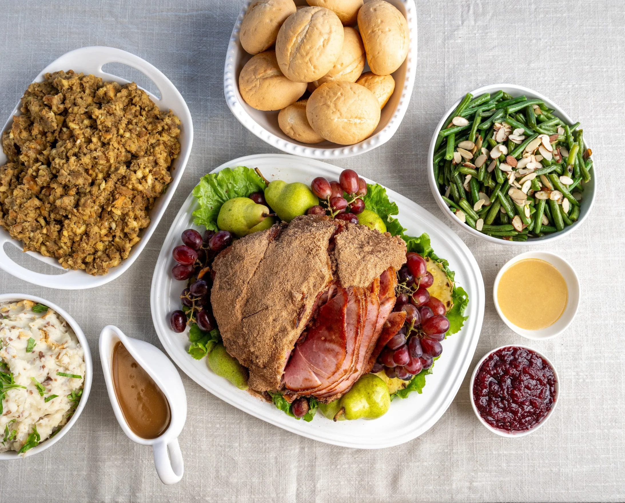 Ham and holiday feast with dinner rolls, ham, gravy, stuffing, green beans, cranberry sauce, and mashed potatoes