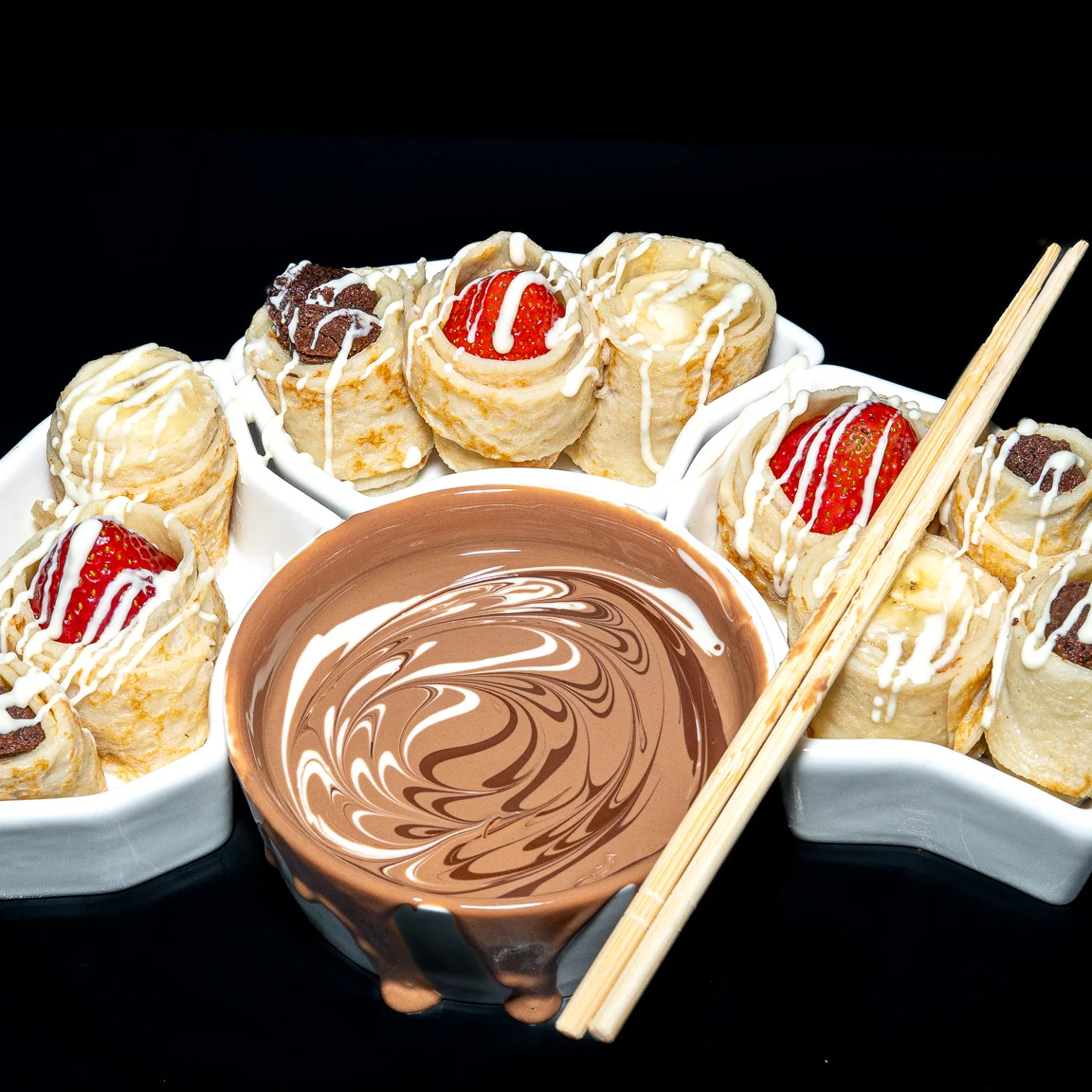 An assortment of fruits including strawberries and bananas drizzled with chocolate and white chocolate on a plate.