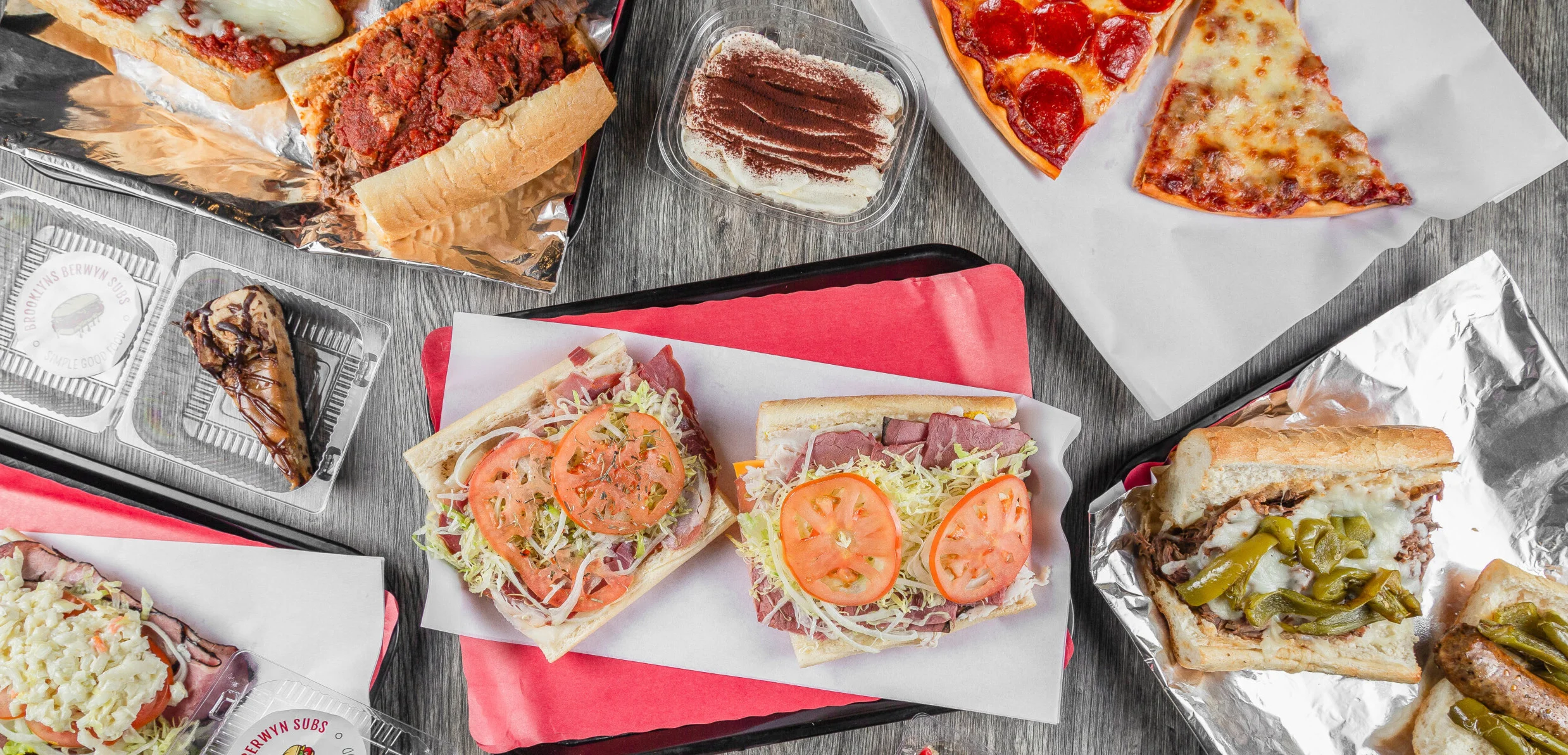 An assortment of delicious food items including sandwiches, pizza slices, and a dessert. The sandwiches are topped with various ingredients and are displayed on trays.