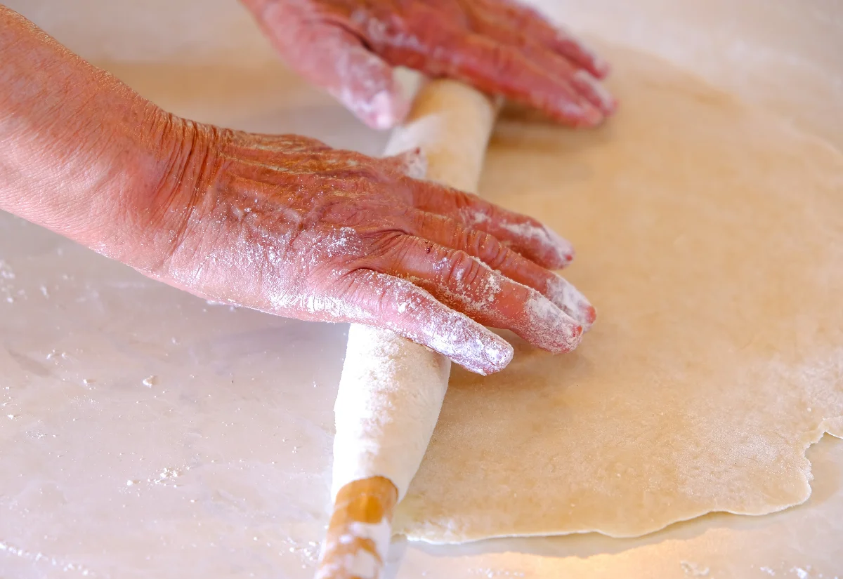 two aged hands rolling out a thin dough