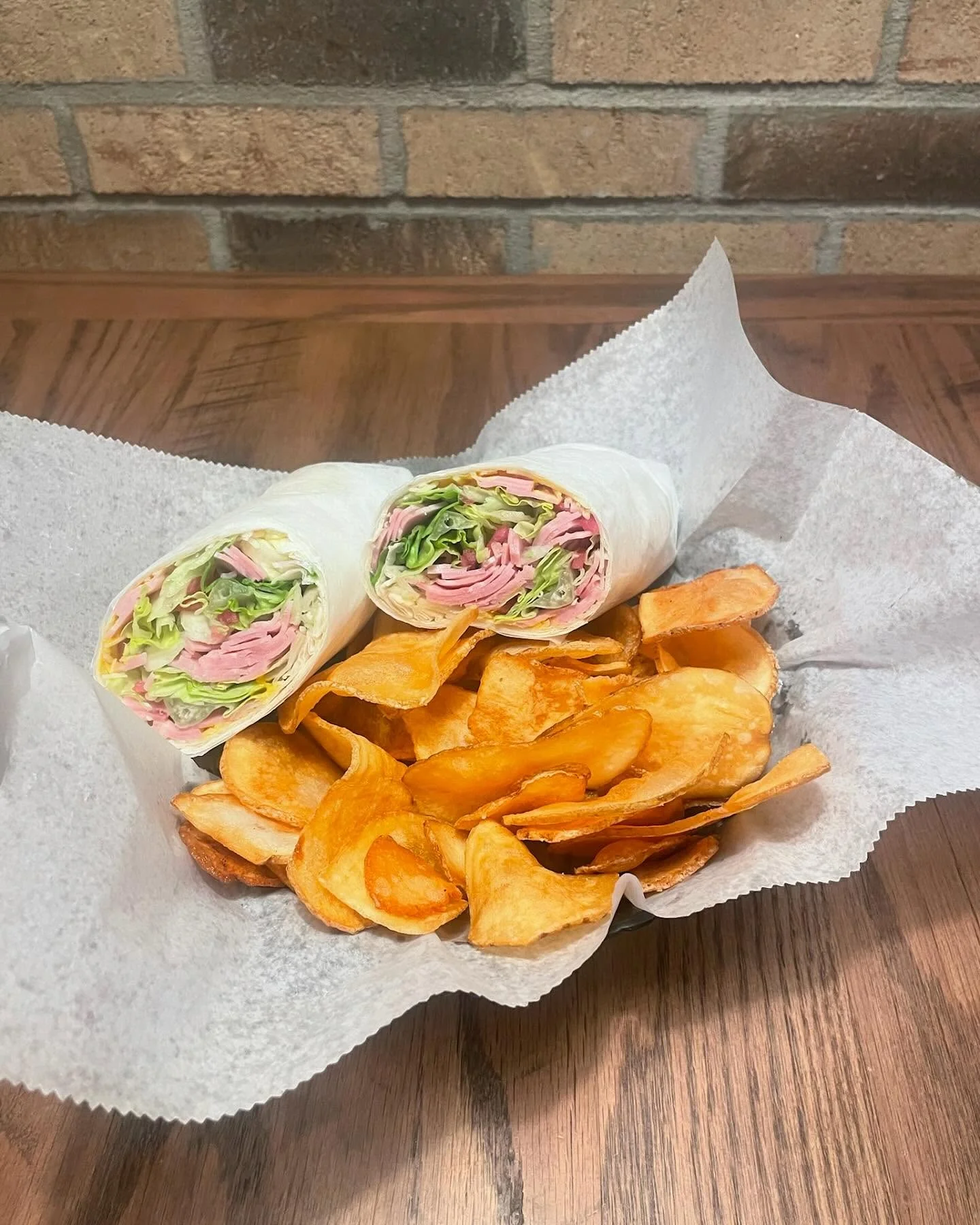 Italian deli wrap with ham and lettuce served with potato chips