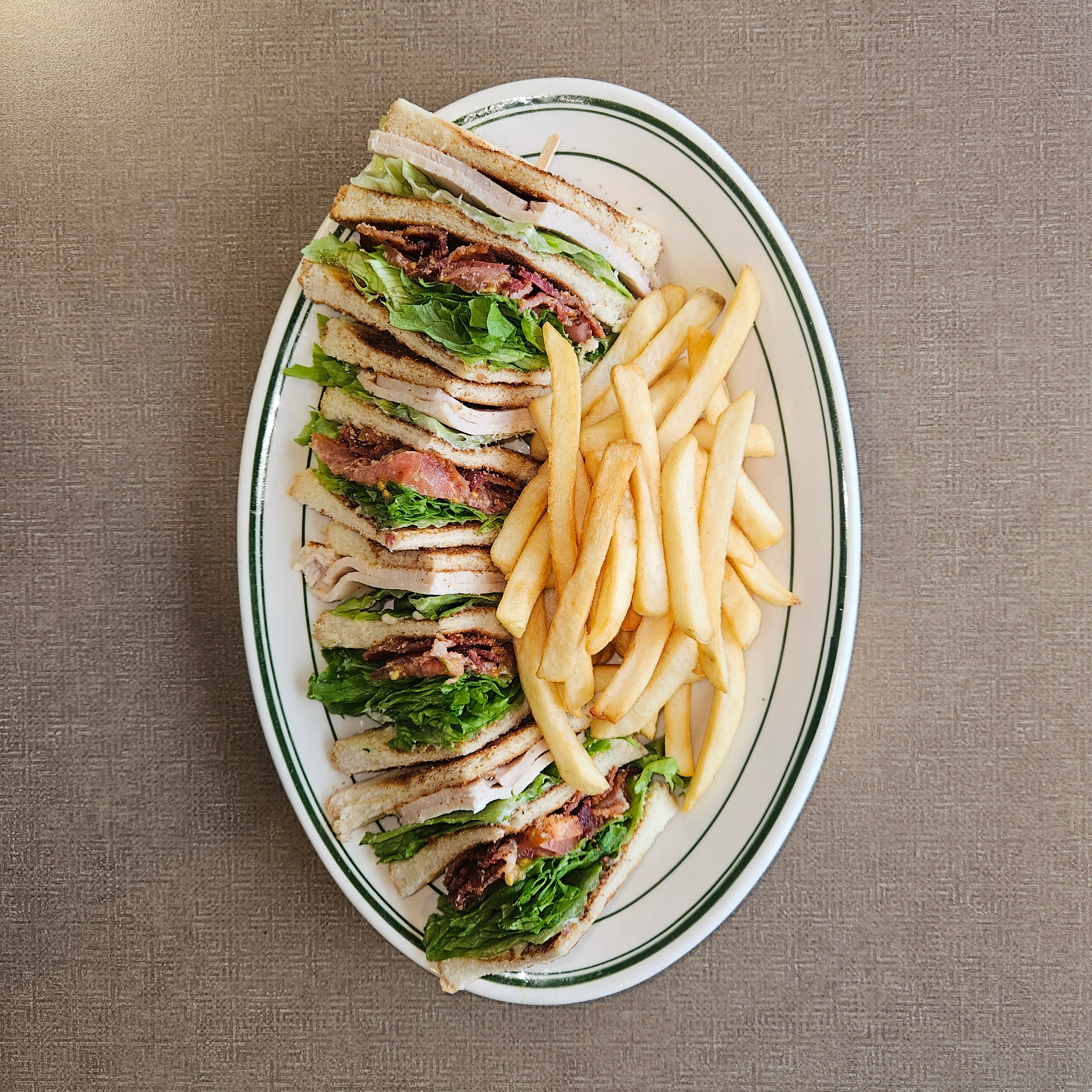 A hearty club sandwich layered with lettuce, bacon, turkey, and tomato, served with a side of golden fries.
