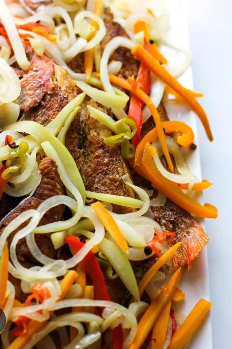 Sautéed fish with colorful bell peppers and onions on a white platter.