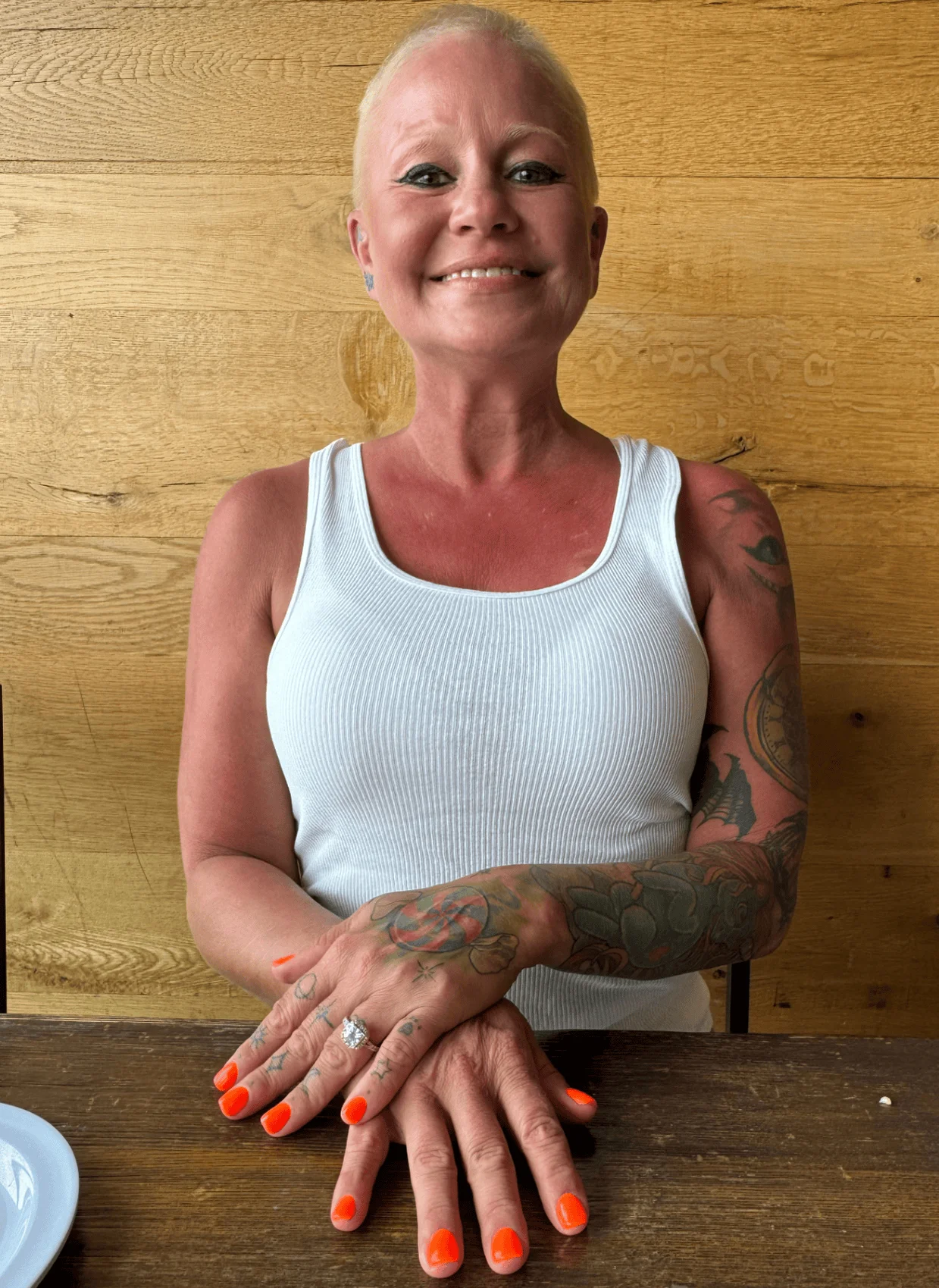 Smiling woman with colorful tattoos and bright nails at a wooden table