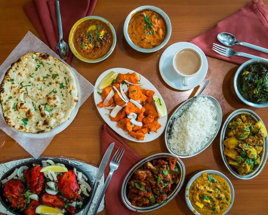 A vibrant spread of Indian cuisine featuring various dishes including naan bread, chicken, rice, and lentils served in bowls alongside a cup of chai.