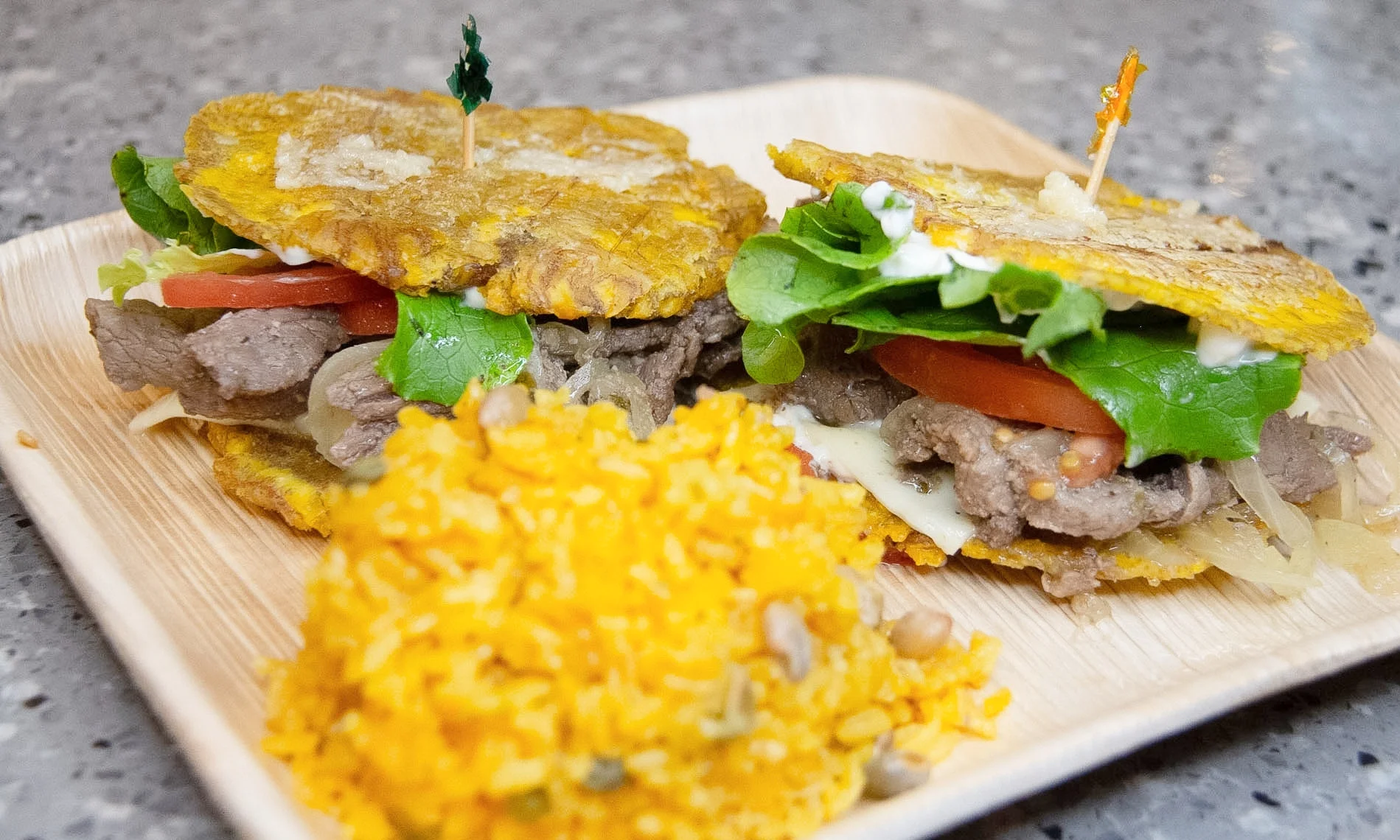 Two servings of beef-stuffed tostones accompanied by yellow rice. The dish includes fresh lettuce, tomatoes, and melted cheese in a vibrant presentation.