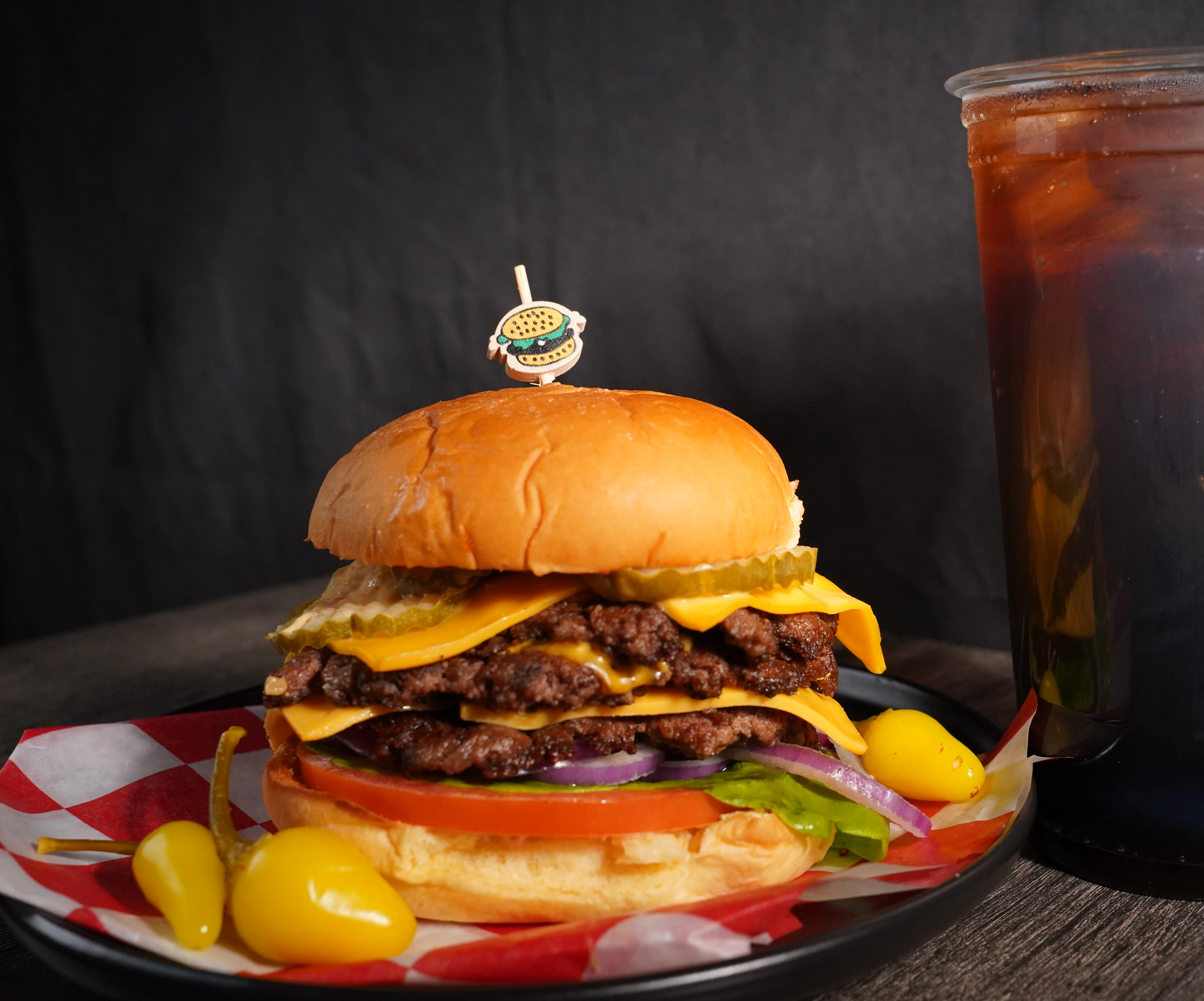A mouthwatering burger topped with jalapeños and cheddar cheese, accompanied by seasoned fries and a refreshing iced drink.