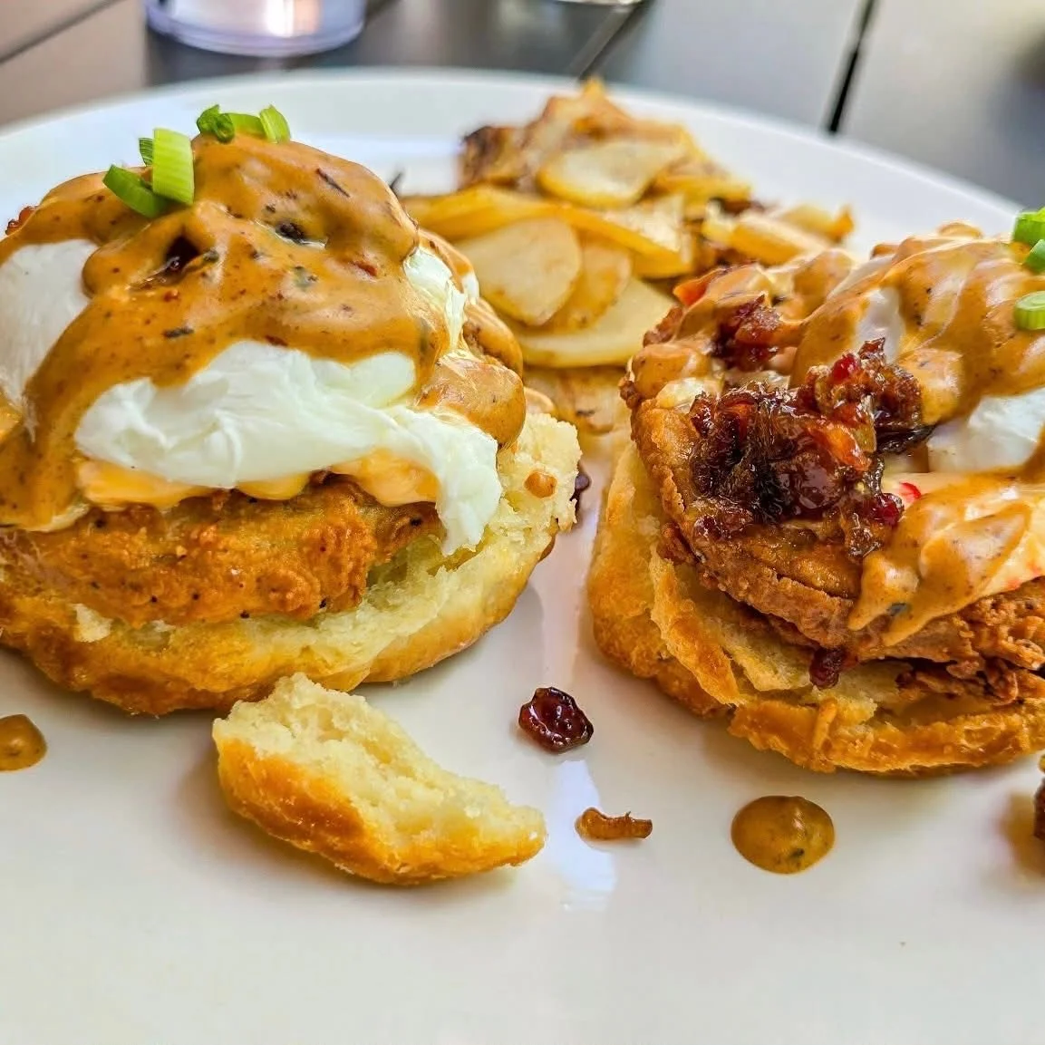 Two chicken biscuits topped with poached eggs and gravy, served with potatoes.