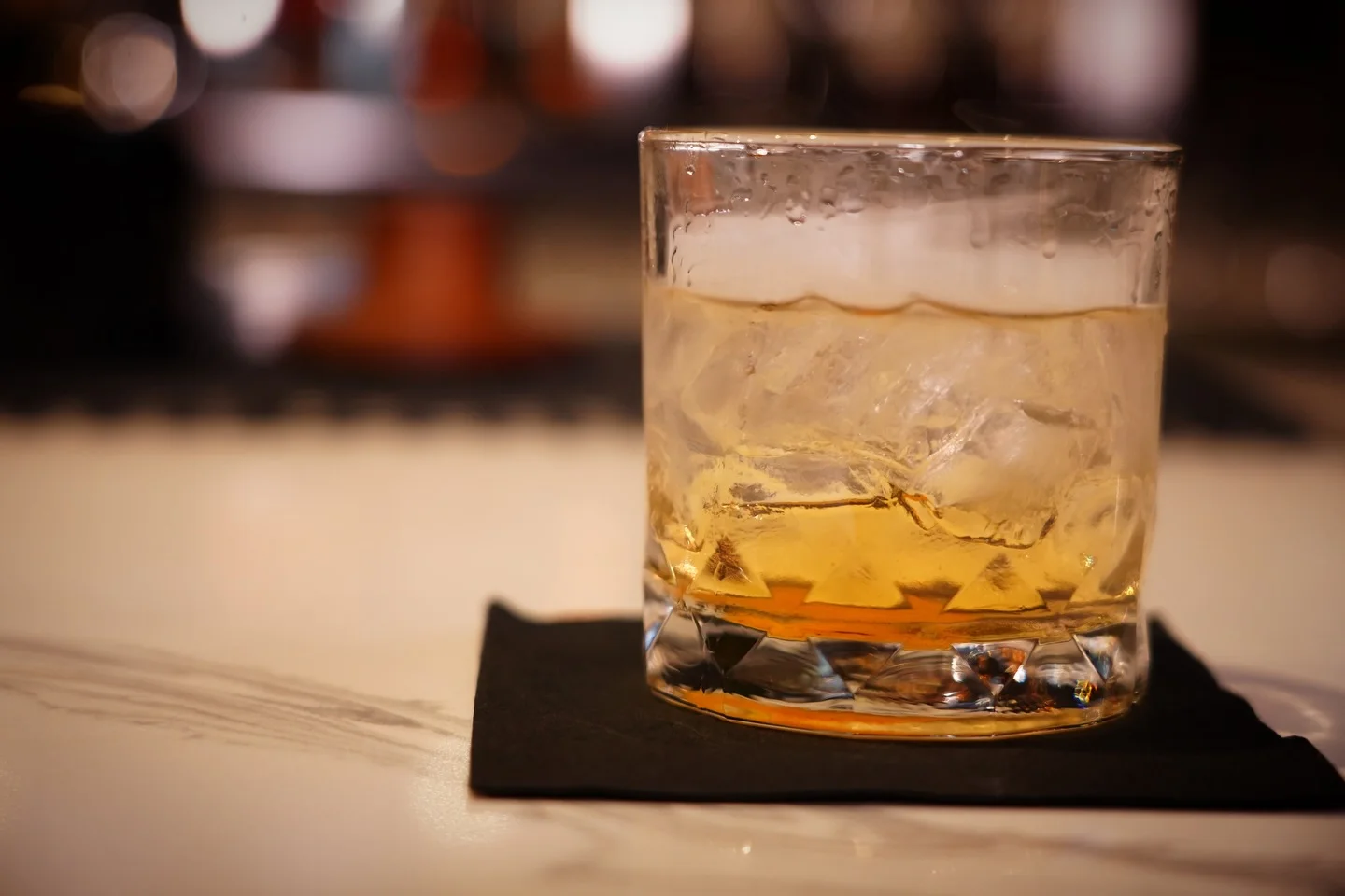 Whiskey cocktail served on a black napkin at a bar