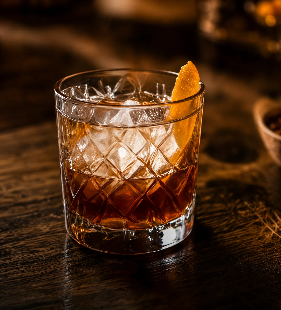 A close-up of an elegant cocktail glass on a wooden surface, filled with a dark drink and garnished with a lemon twist.