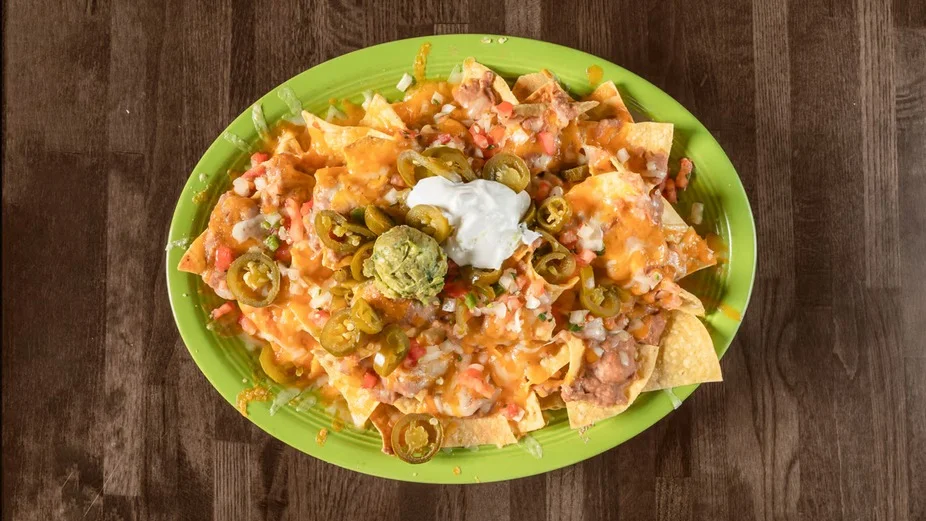 A colorful platter of nachos topped with cheese, jalapeños, pico de gallo, and a dollop of sour cream, served on a green plate.