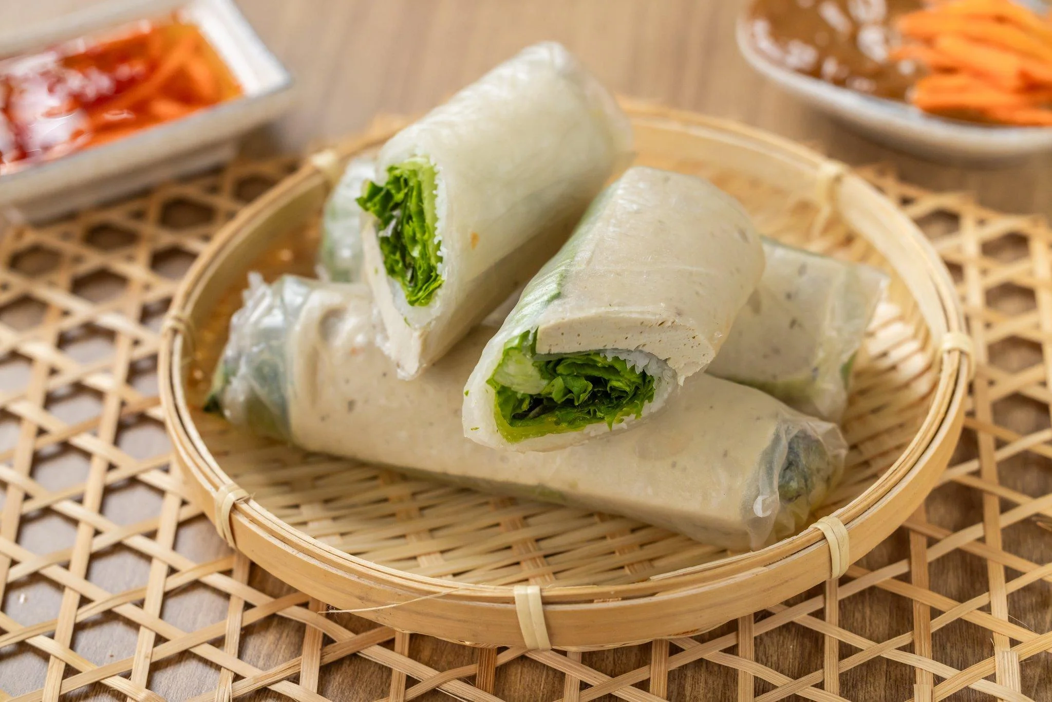 Fresh spring rolls filled with lettuce and other ingredients. They are neatly placed in a round bamboo basket.
