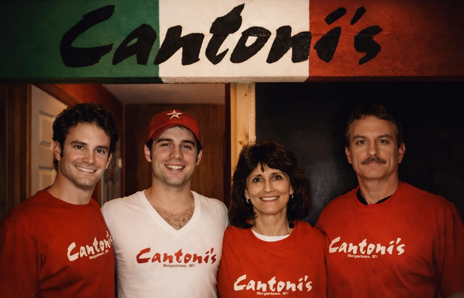 A family posing in front of the entrance of a pizzeria, wearing matching red shirts, exuding a friendly vibe.