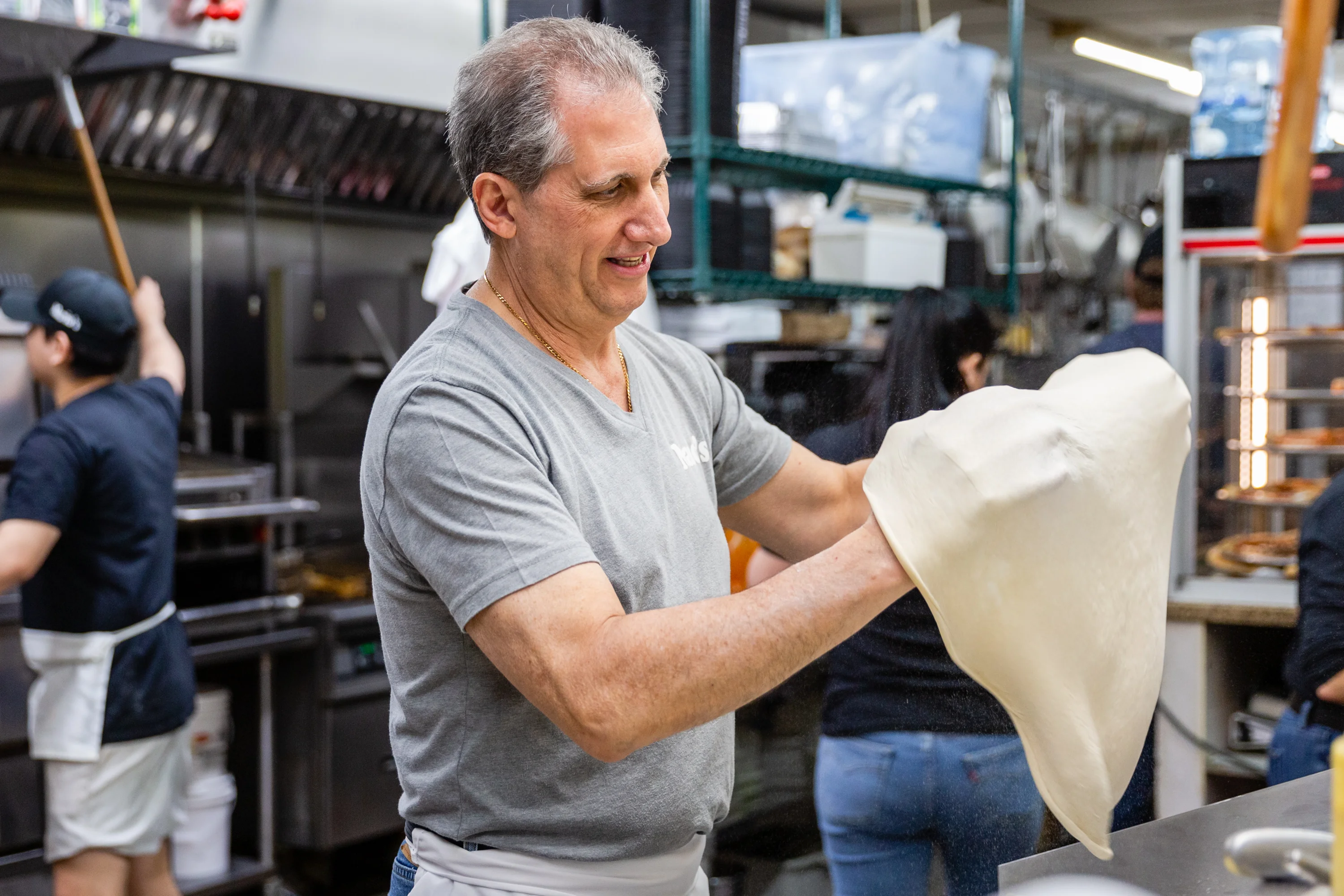 Chef tossing pizza dough in a busy kitchen