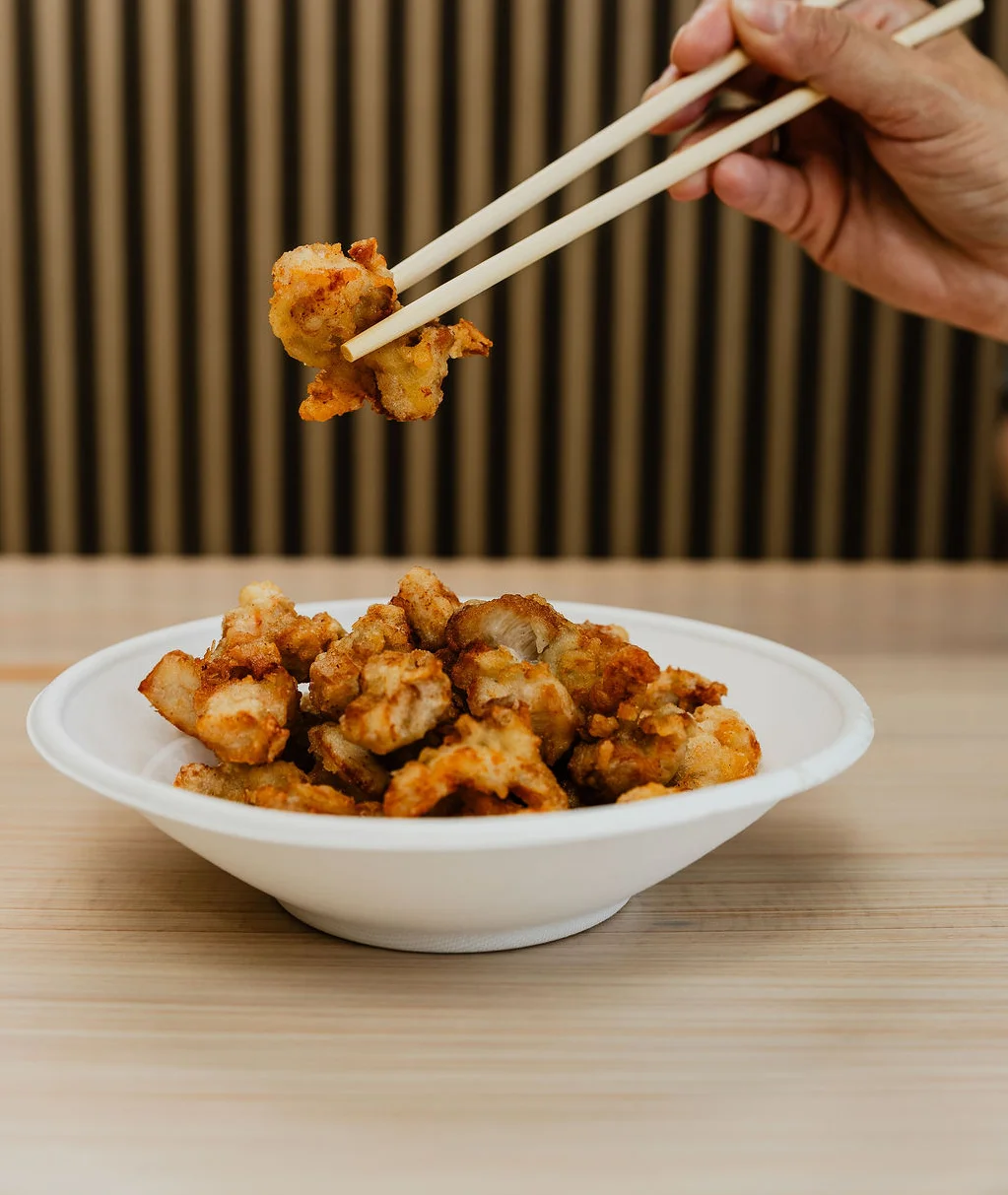 a hand holding up a chunk of crispy fried chicken with chopsticks