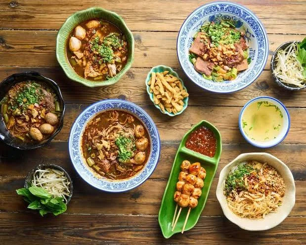 Assorted bowls of Thai boat noodles with skewers and condiments