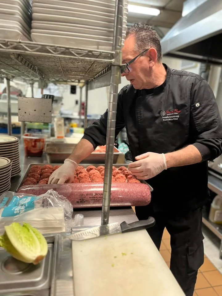 A chef preparing ground meat in a well-equipped kitchen, wearing gloves and focusing on the task at hand.