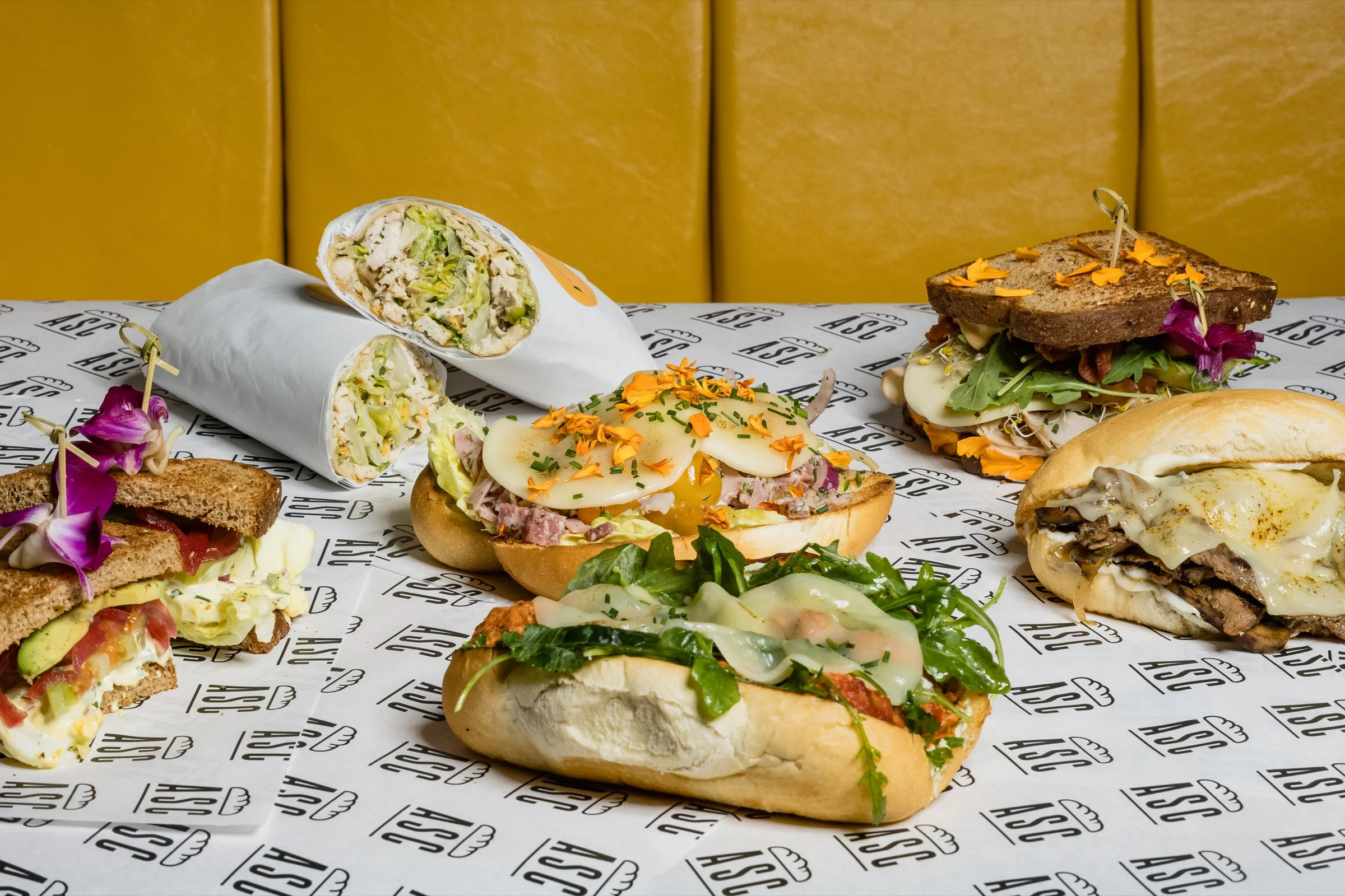 A colorful spread of A Sandwich Co. sandwiches and wraps on branded paper