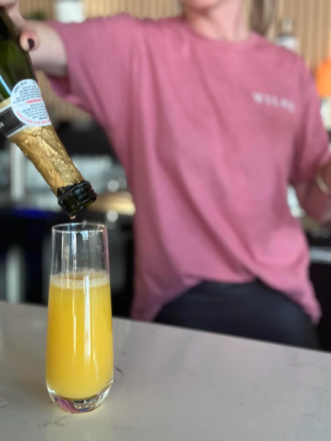 Bartender pouring mimosa into a glass at a stylish bar