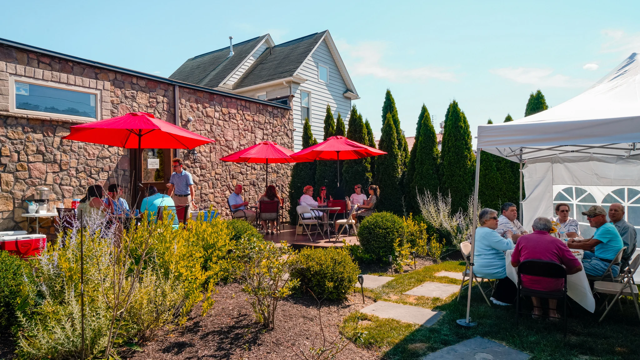 Outdoor dining area with red umbrellas and guests enjoying a sunny day